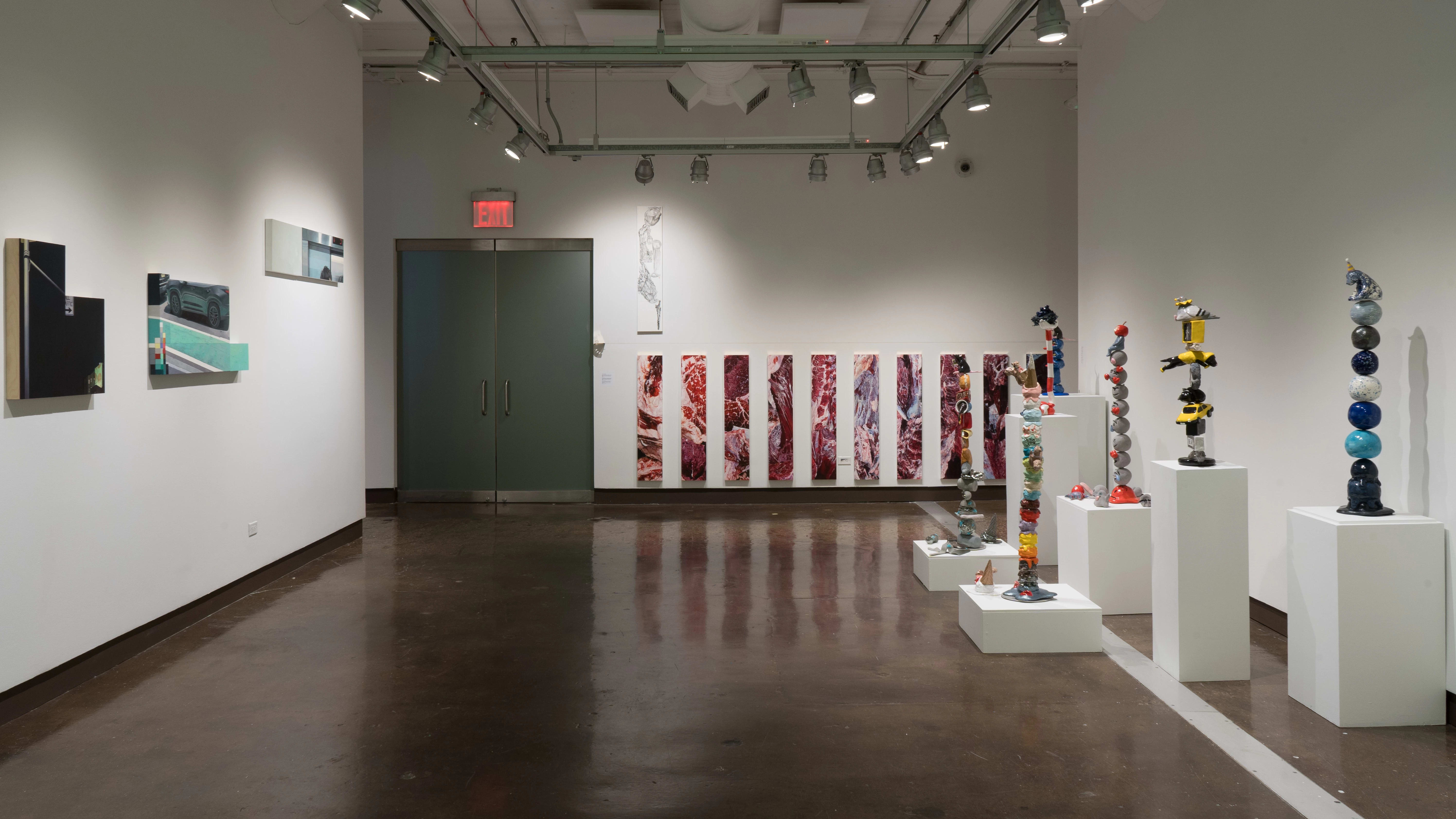 On the far wall in gallery two, narrow, vertical paintings that look like raw meat are hung in a row. On the left wall are the paintings that seem to be cut from a whole, and on the right are several pedestals displaying ceramic sculptures of objects stacked precariously high.