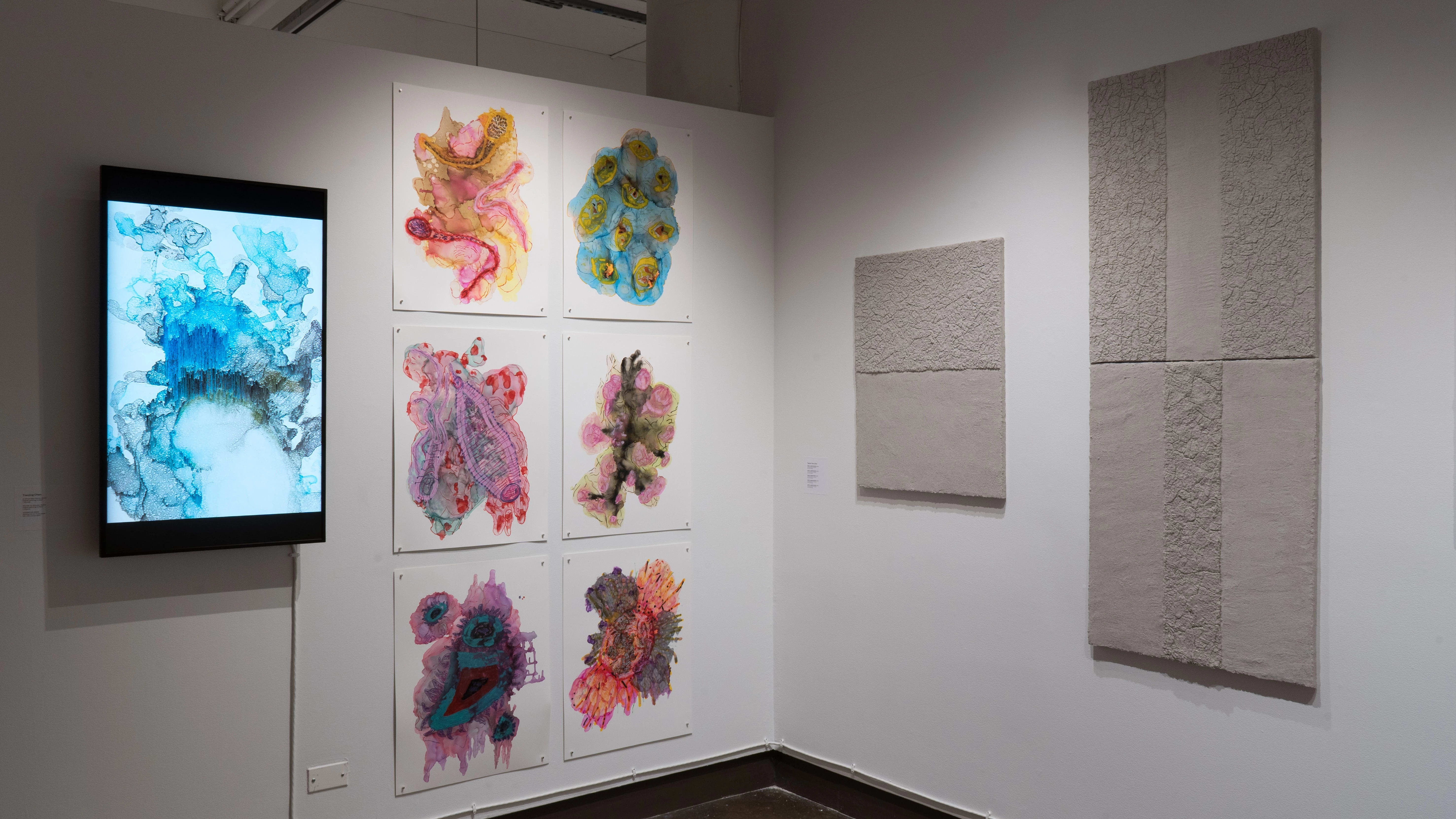 The alcove of gallery four holds what looks like textured cement blocks mounted on one of the walls. Bright, abstract watercolors and a colorful animation on a monitor juxtapose the concrete works on the adjacent wall.