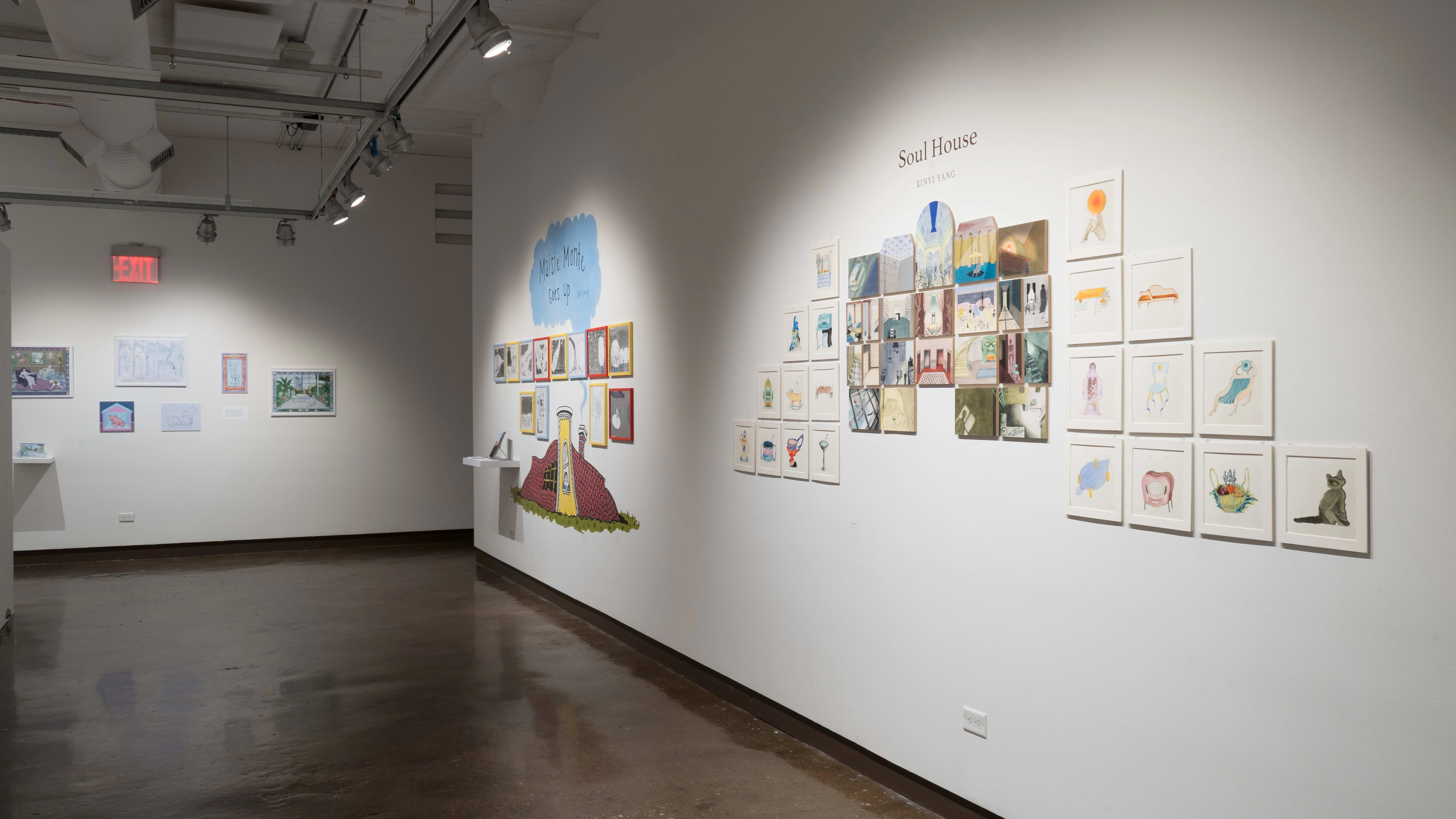 Many small, framed illustrations are arranged into a pyramid shape on a wall of gallery three. To the left, a small cottage is painted on the wall with framed illustrations organized around it.