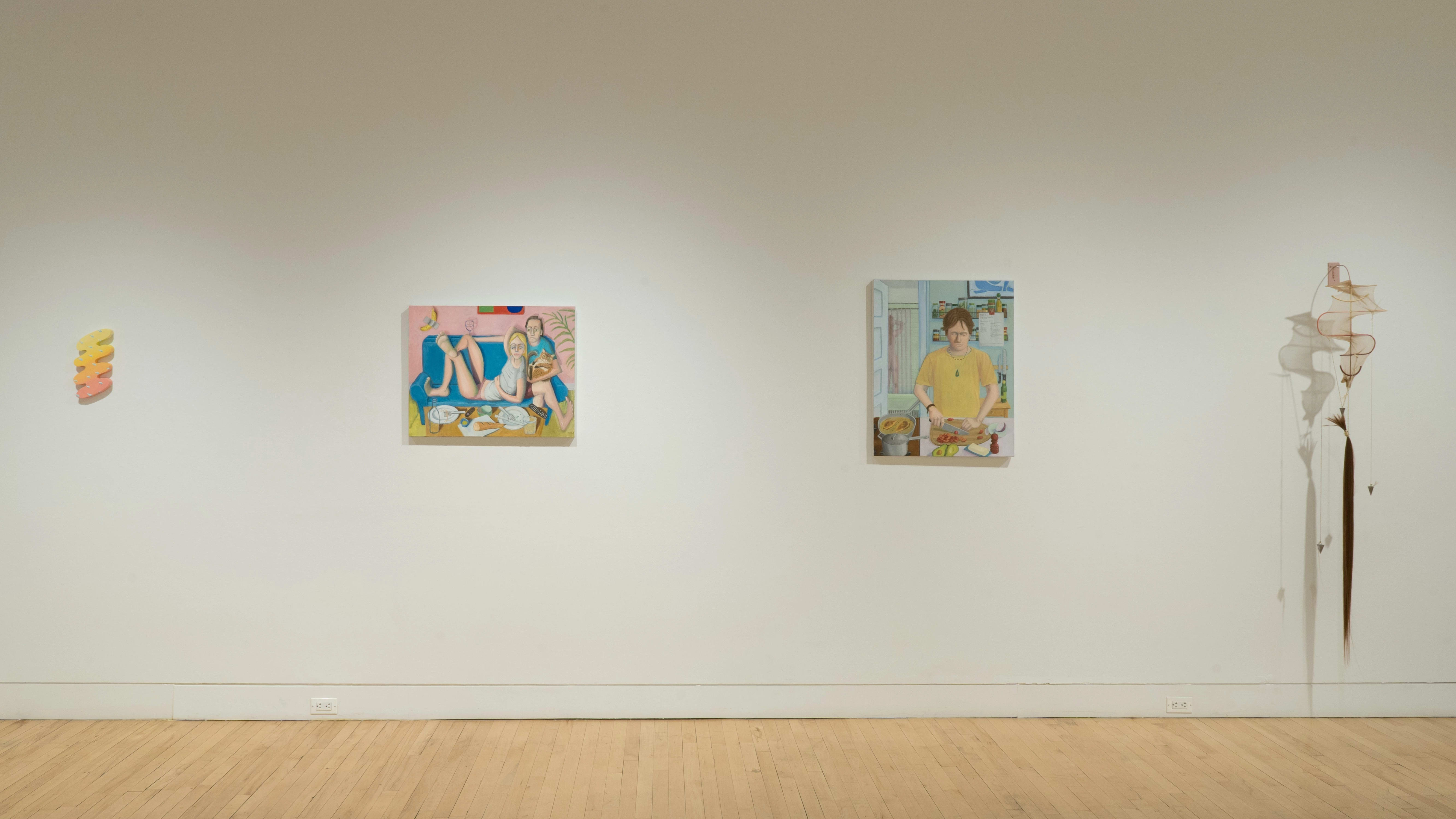 On one gallery wall, there is a pink and yellow painting on a small, squiggle-shaped panel. To the right, there are two figurative paintings in the same style. On the far right, a sculpture on the wall appears to be a long string of hair tied to a piece of metal covered with pantyhose.