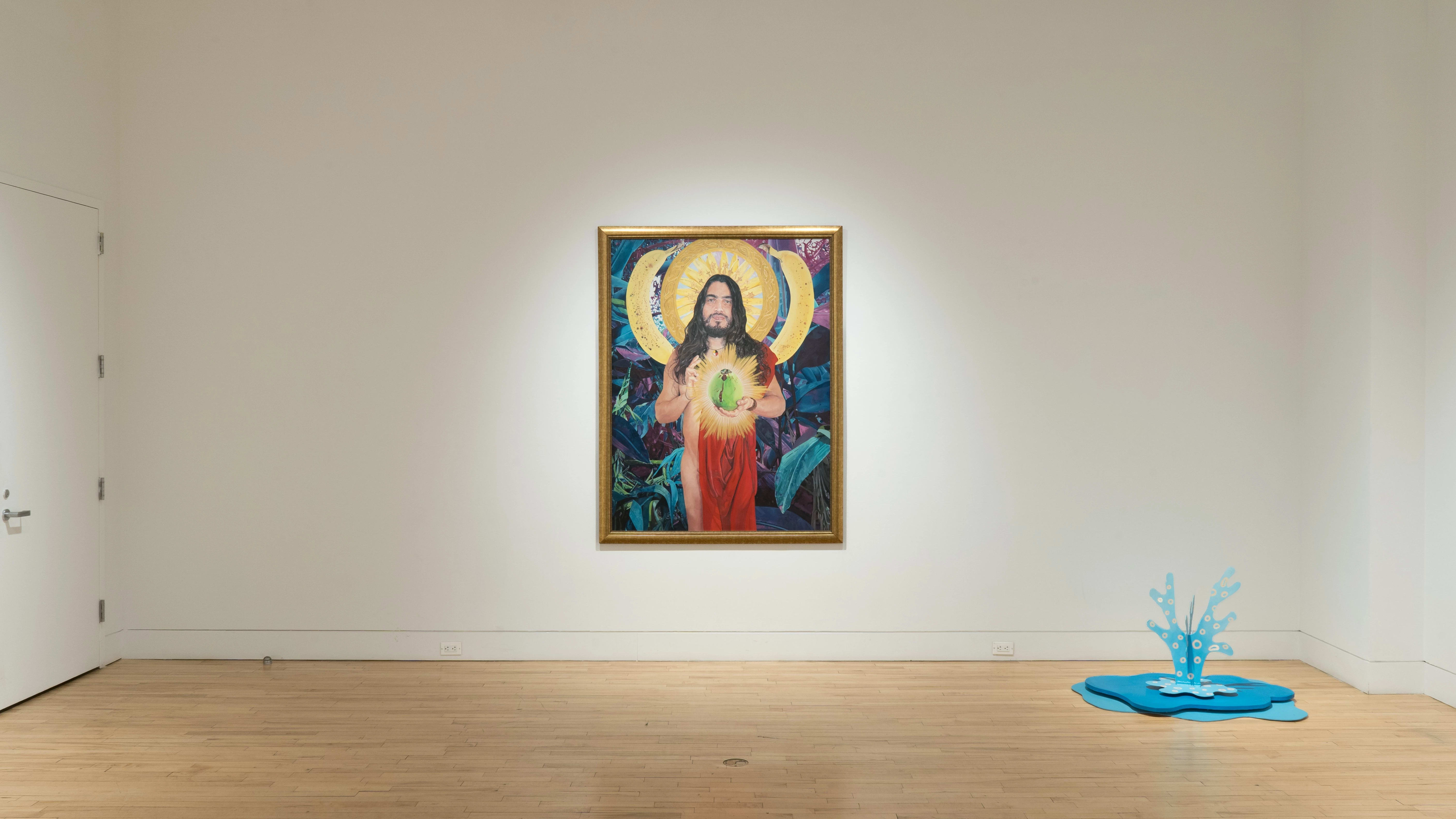 In a corner of the gallery, there is a sculpture of a blue fountain sitting on the ground. On the wall behind it, there is a very large painting of a saint-like person in a gold frame.