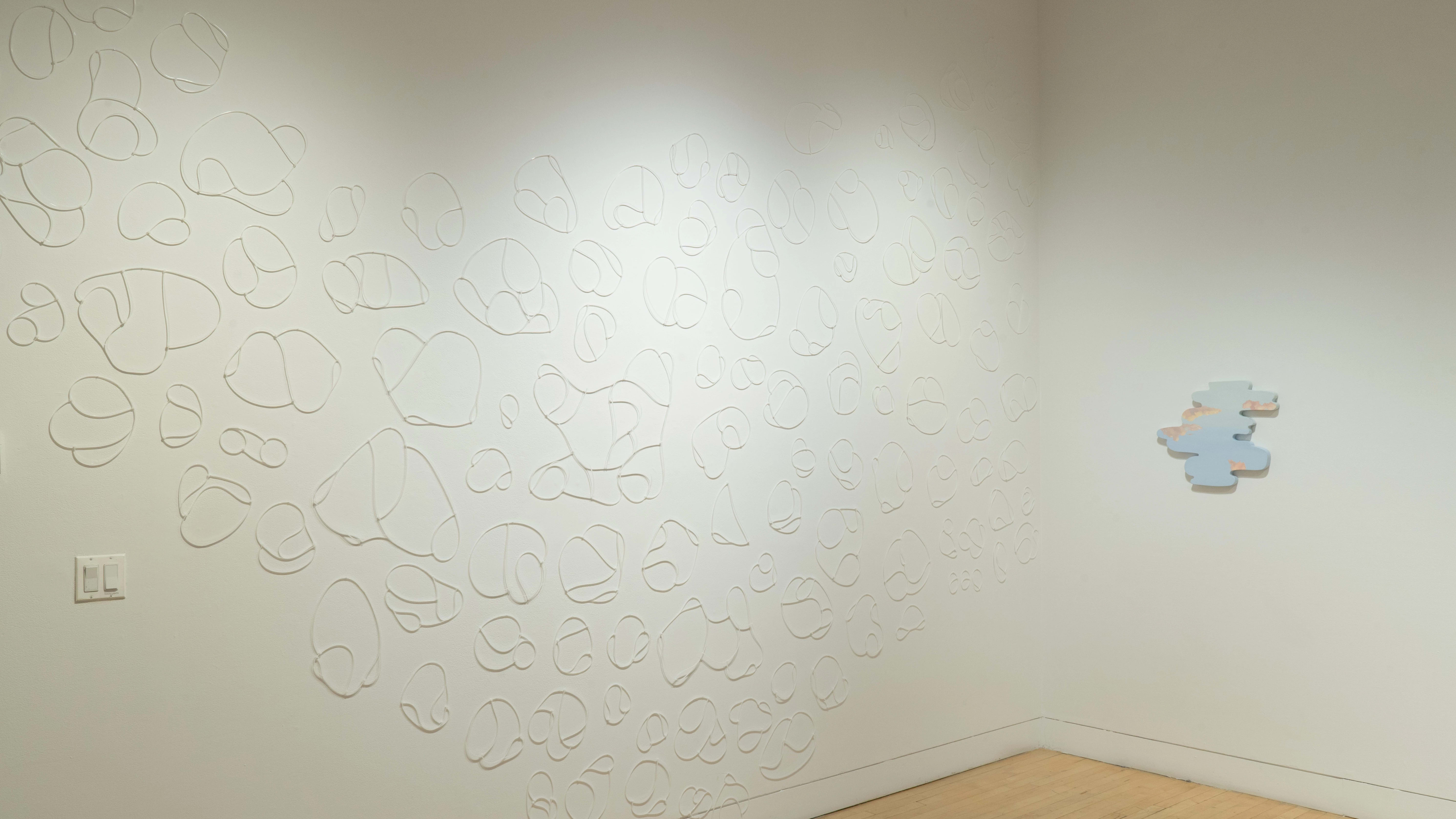 Inside the gallery, zip ties in organic shapes cover a wall. To the right, a pastel sky is painted on an organic-shaped panel.