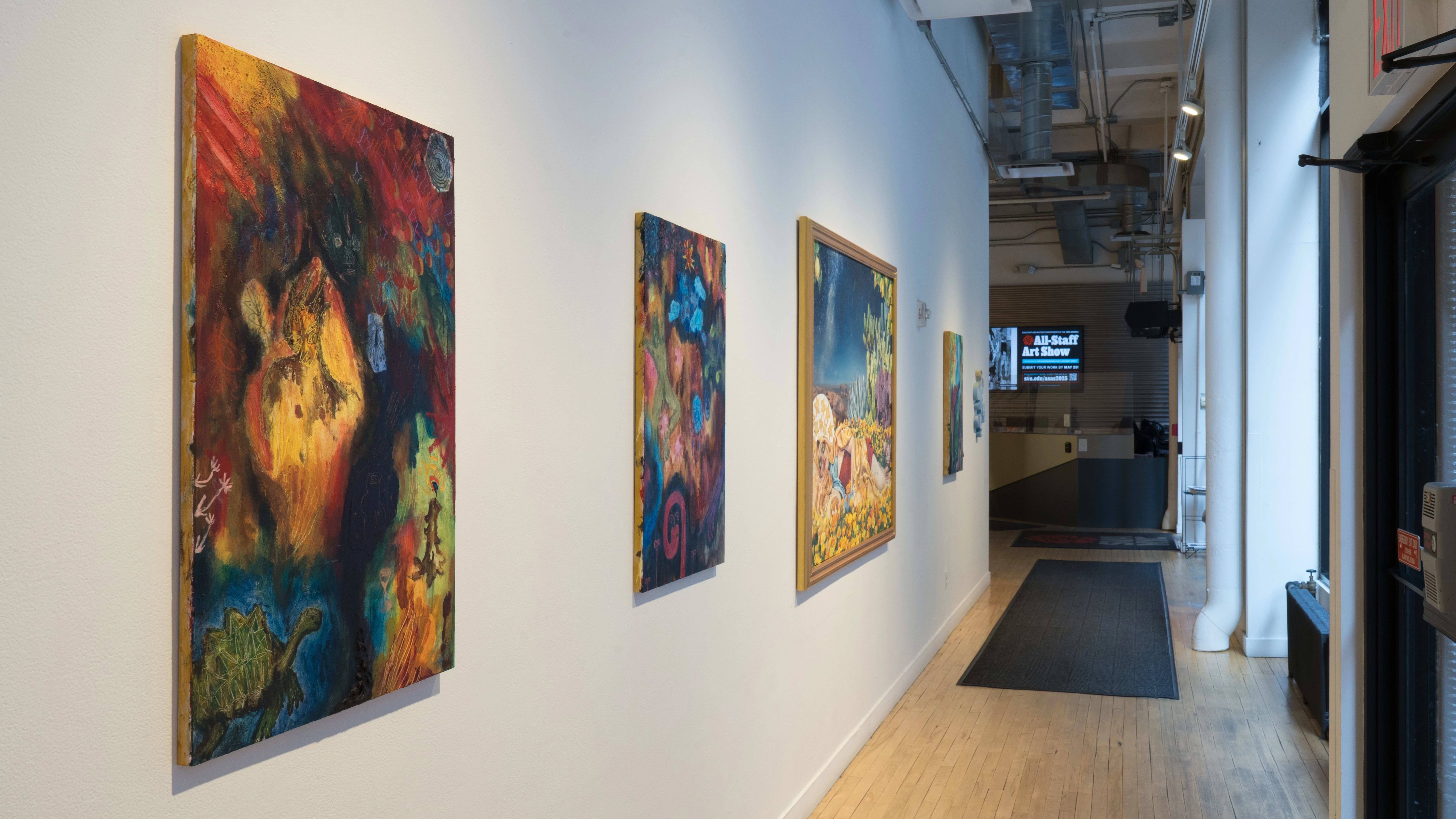 Inside the SVA Flatiron Windows hallway, two portrait-oriented colorful paintings hang beside a large, framed, landscape-oriented painting. More works hang further down the wall.