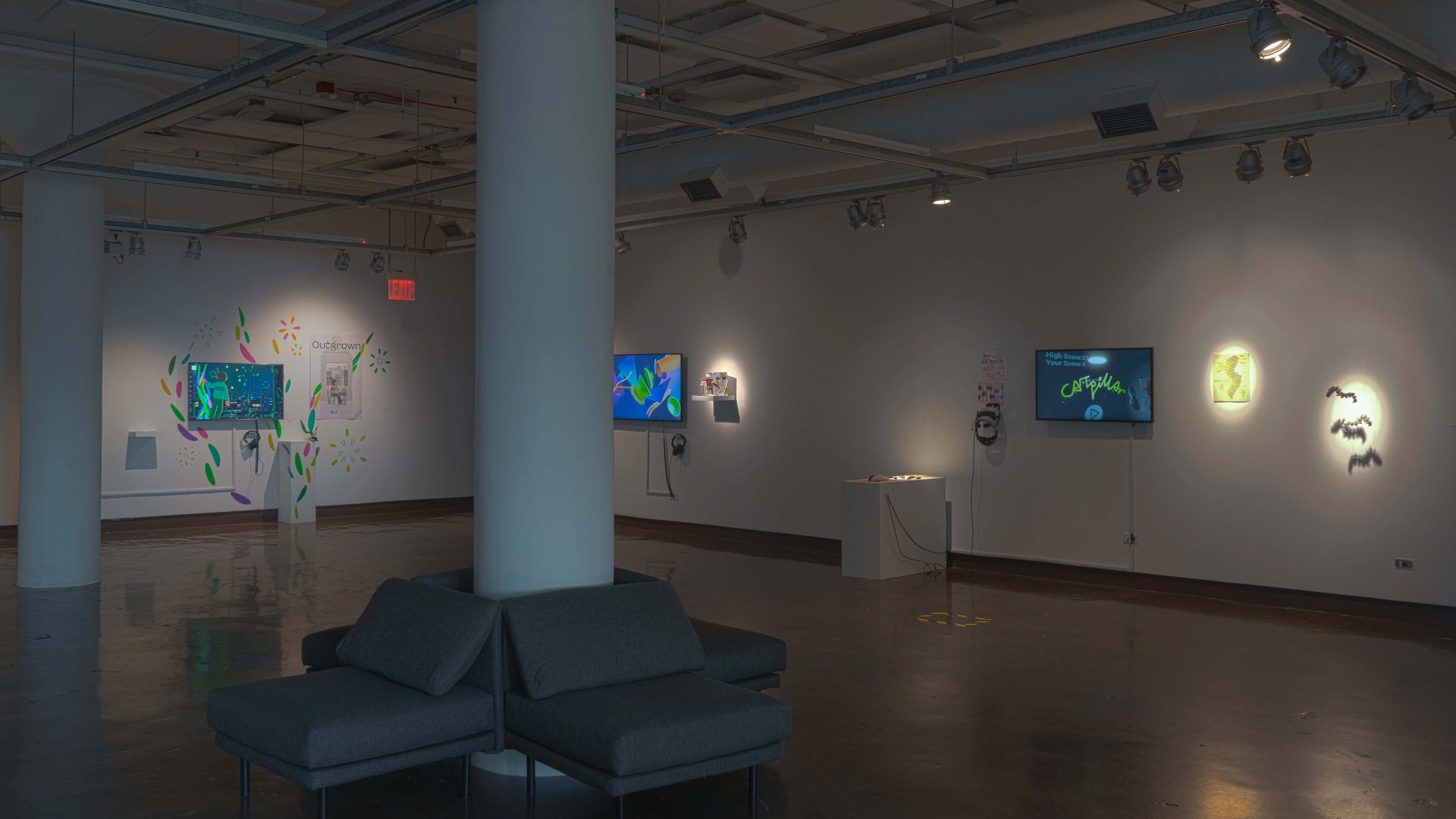 Several monitors on the walls play animated videos in gallery one of the SVA Chelsea Gallery. Each monitor is accompanied by prints and objects, such as small sculptures or dioramas.