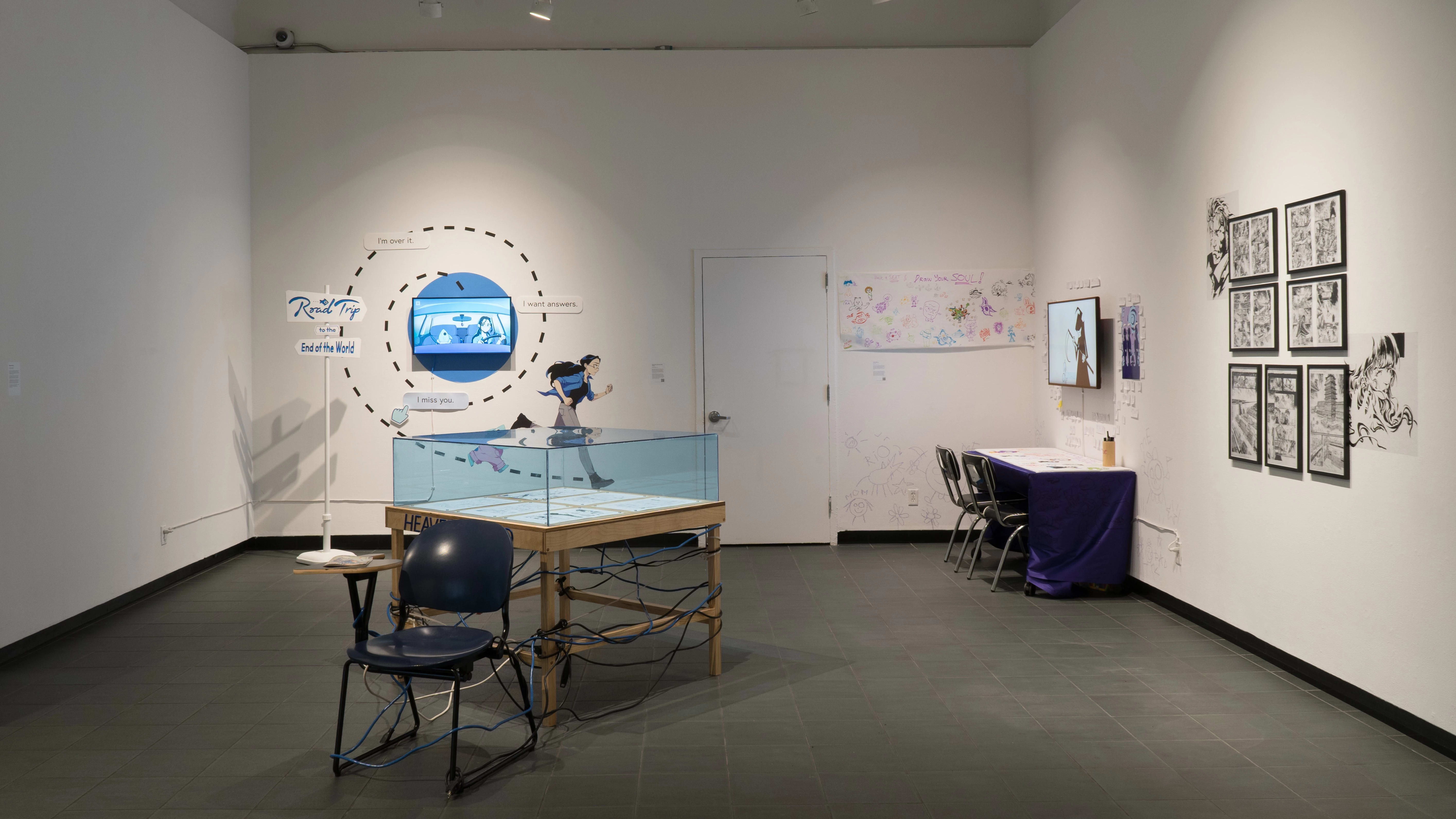 Several works in the ‘Now and Then exhibition. In the front is a glass display on a wooden table, with artworks present inside. Behind that are two animations by students and frames featuring black and white comic panels.