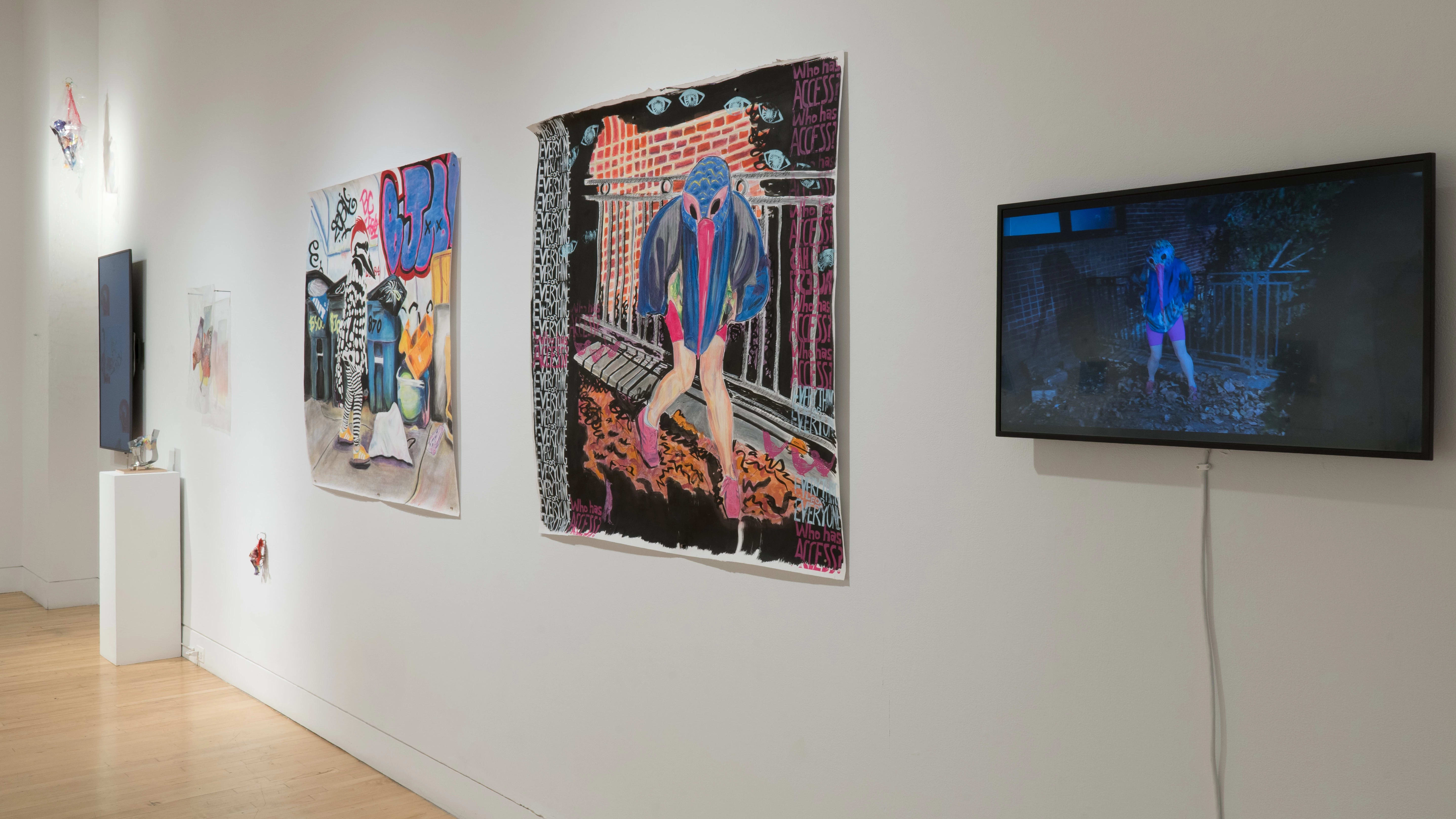 Along one wall of the gallery, a small monitor is on display next to two large square paintings of humans with bird heads. Beyond them, a vertical monitor is surrounded by small colorful sculptures made of plastic detritus.