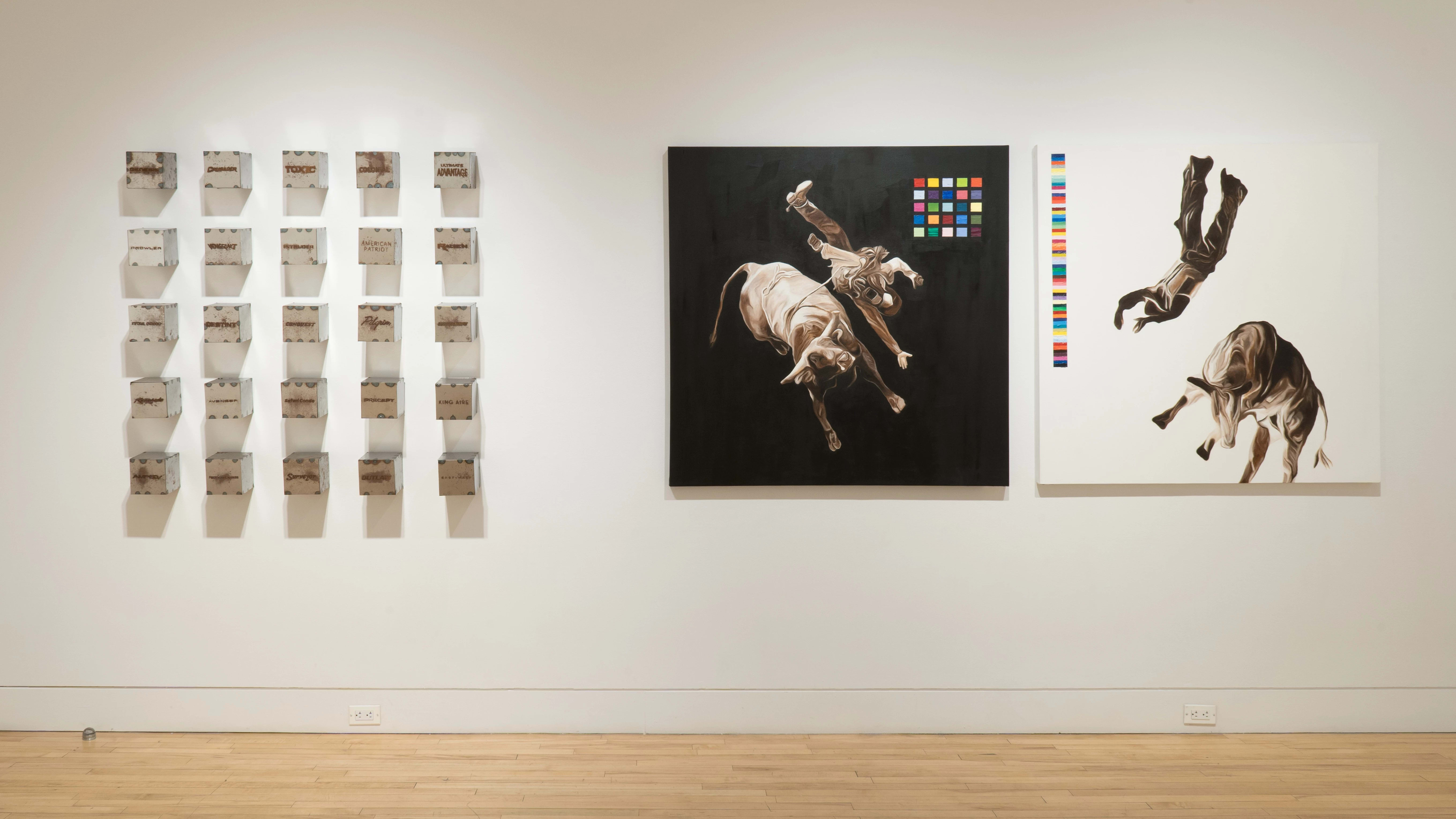 Two large, square paintings on canvas hang beside each other on one of the gallery walls. One has a black background, and one has a white background, but both depict a cowboy and a cow seemingly falling into nothingness. To the left, silver cubes are mounted on the wall in a 5 x 5 grid.