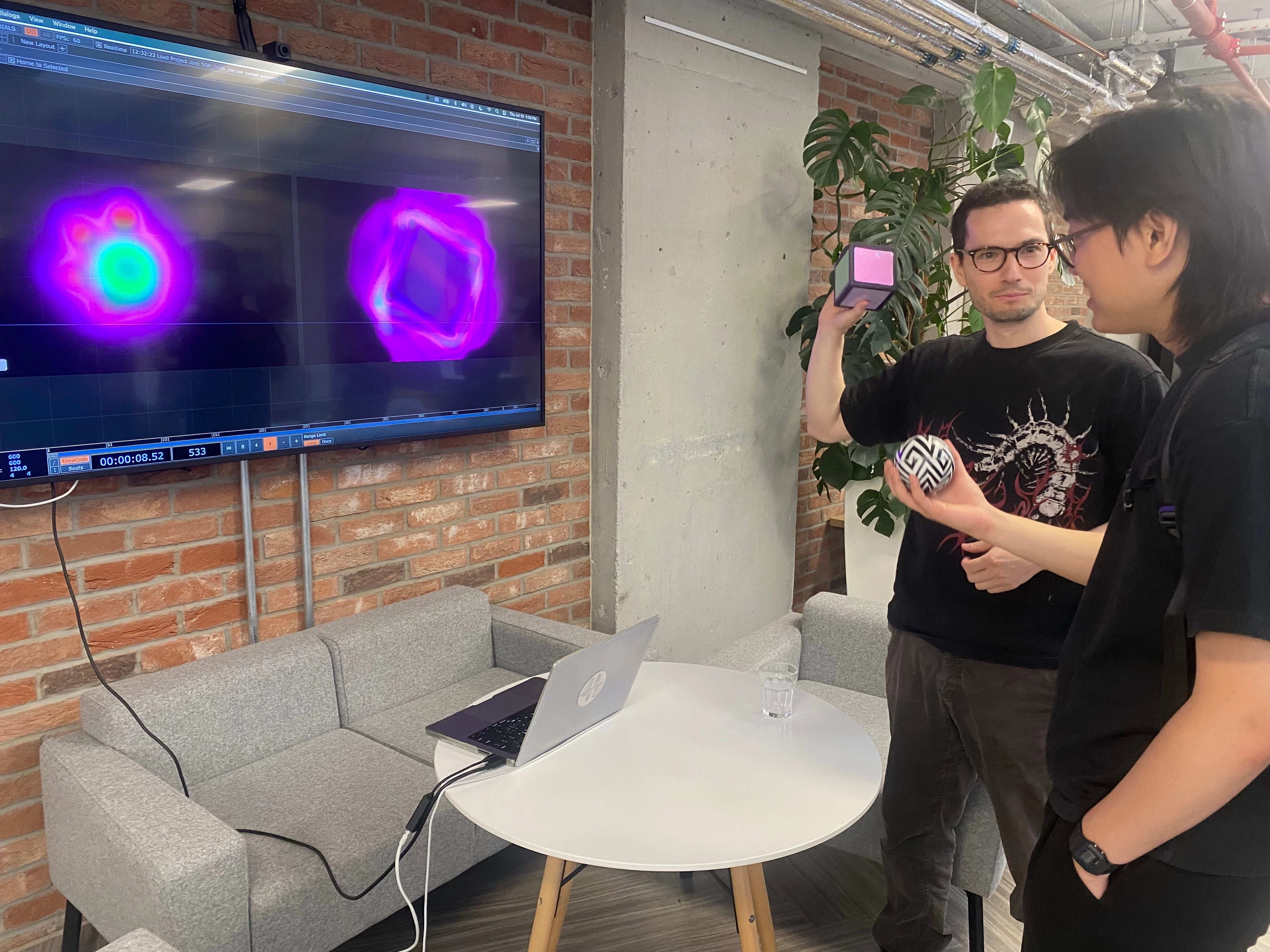 Two people hold toys as they watch the interactive elements perform on a TV in fron t of them.