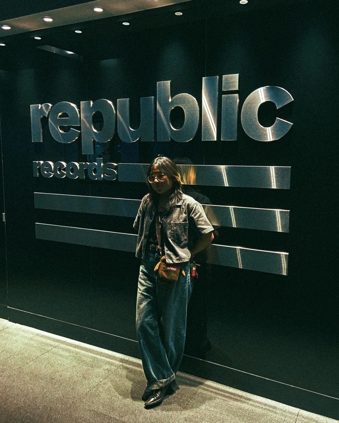 Student leans against large metallic Republic Records logo on wall.