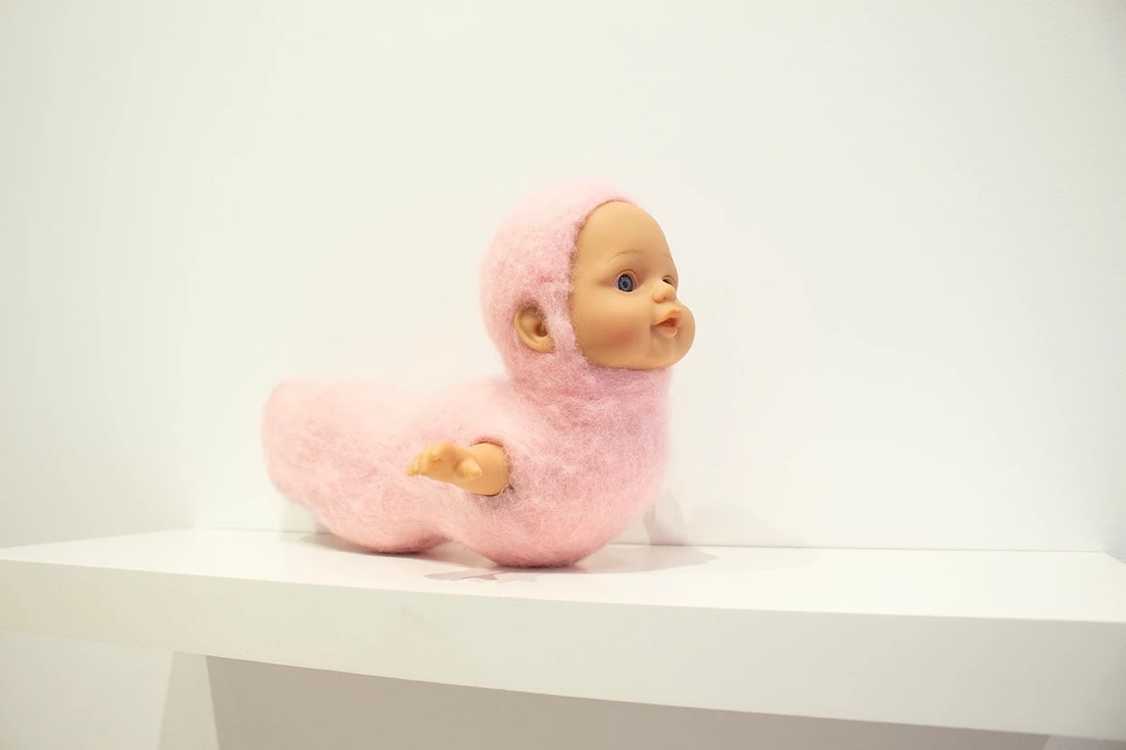Fuzzy pink sculpture of a baby's head and worm body.