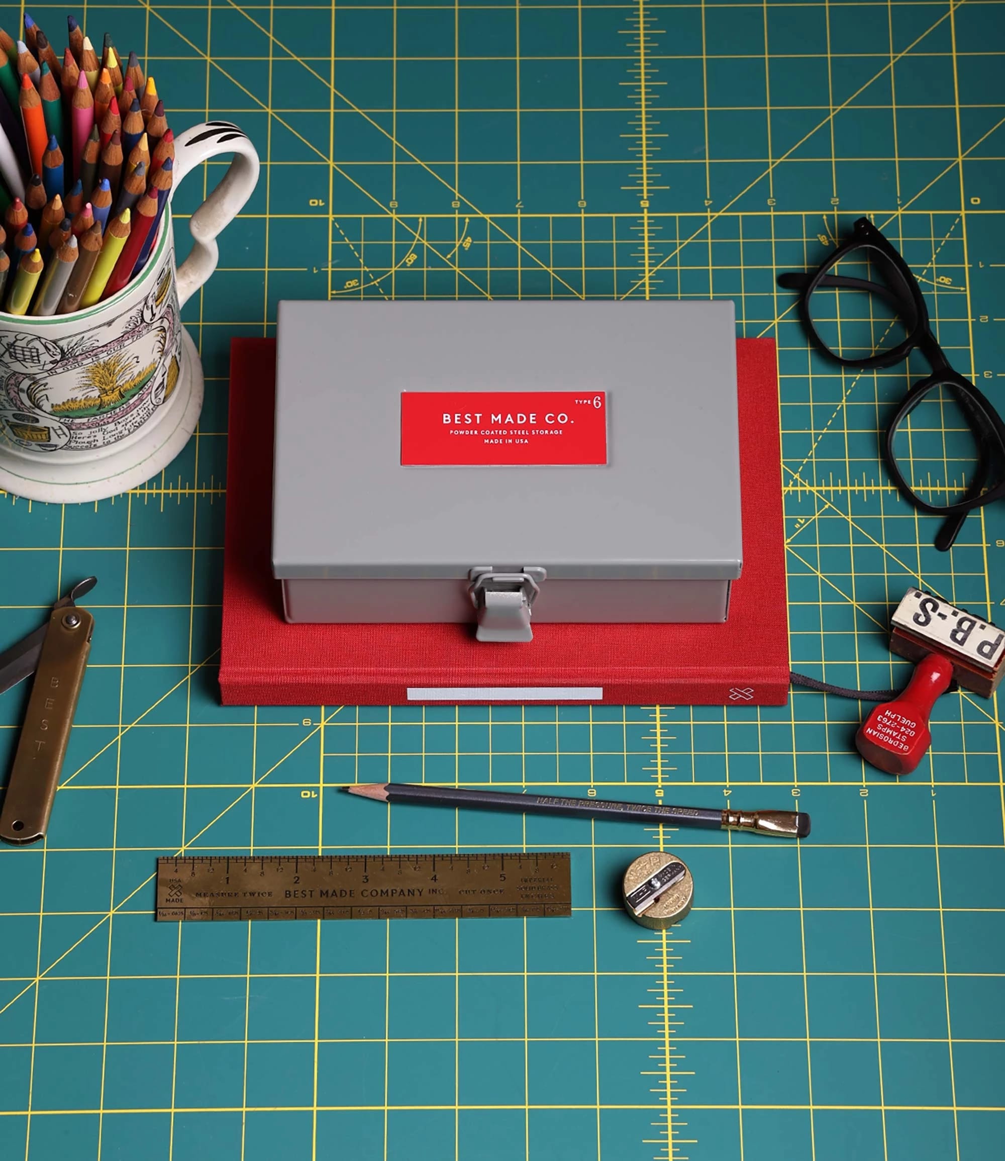 A workspace featuring a box of pencils, a cup of coffee, a ruler, and scissors on a table.