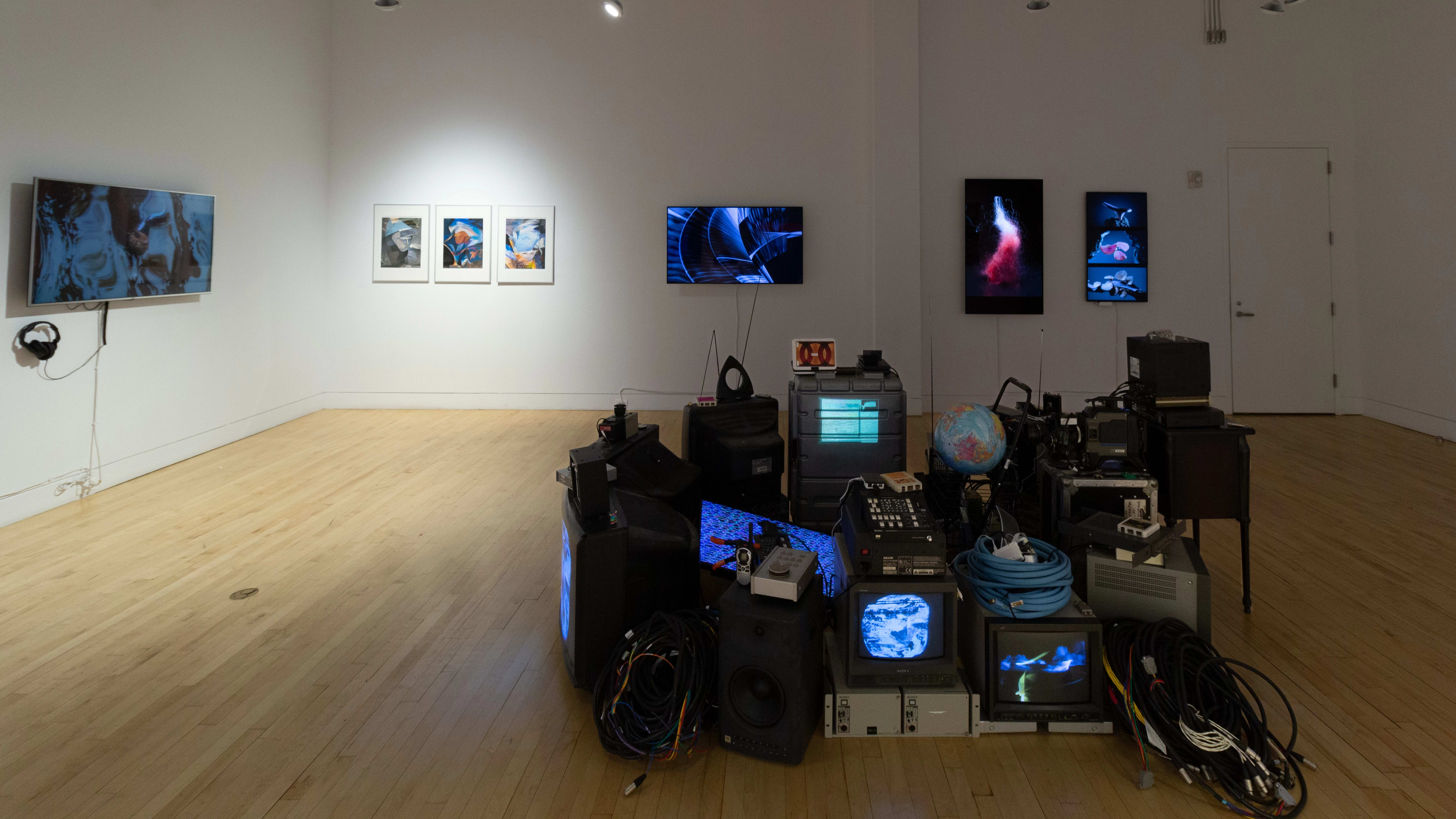 Another view of the gallery in which the work of MFA Computer Arts students is displayed. As a part of the installation in the center of the room, a globe appears on an old tv set, and a physical globe sits atop the pile of materials.