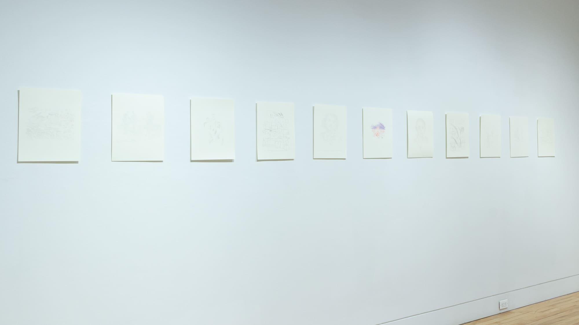 Photograph of small works on letter-sized white paper, each containing very lightly colored drawings.