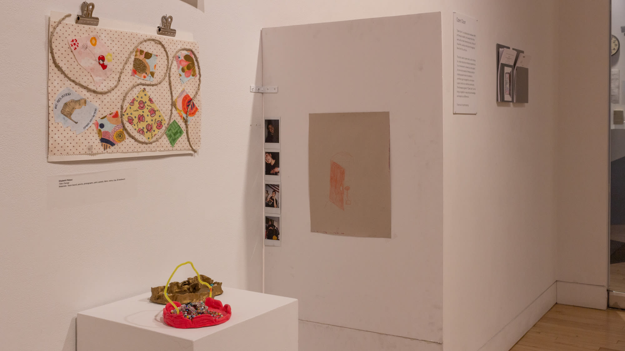 A variety of artworks by Art Therapy students against a white wall in gallery space.