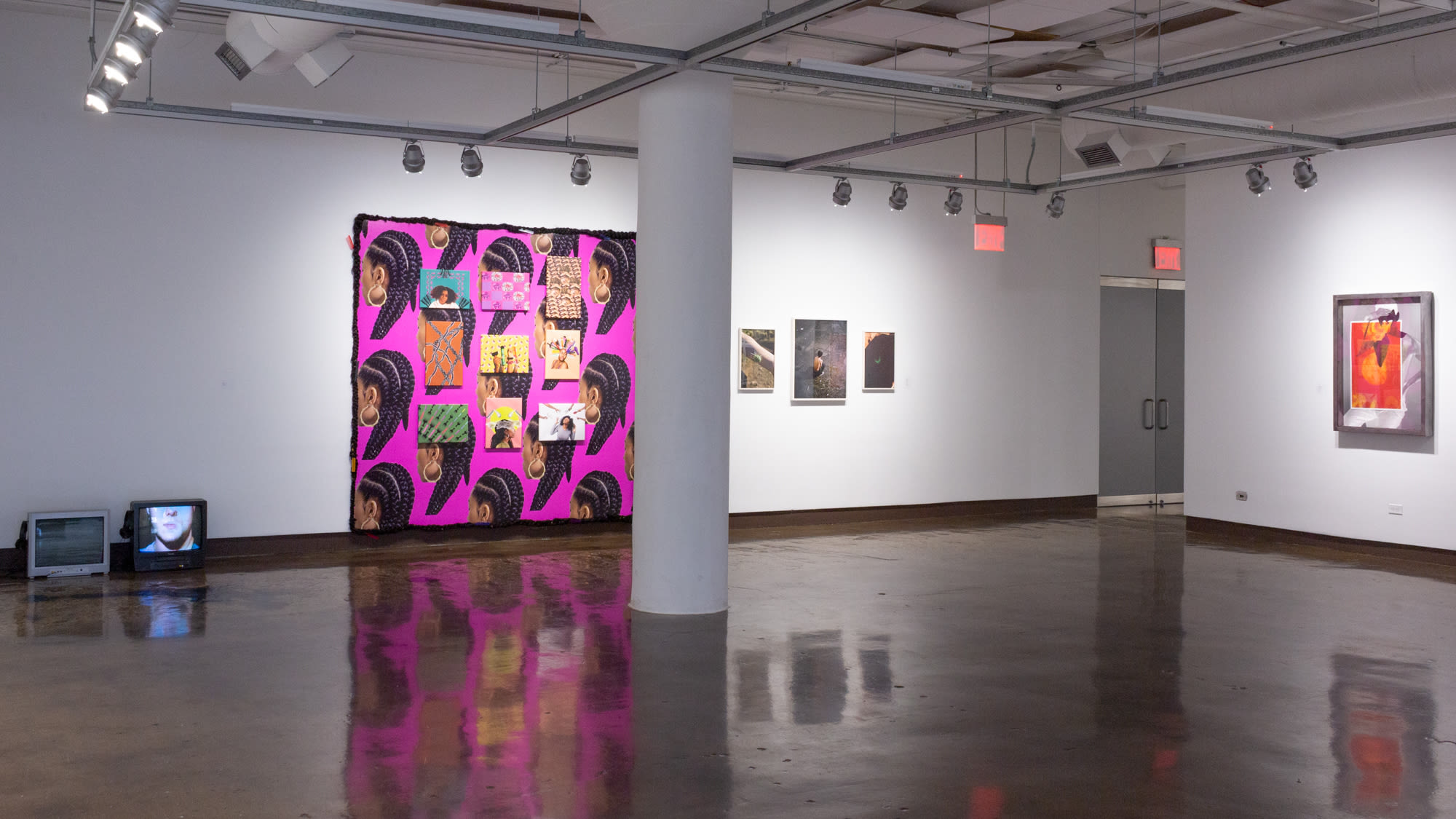 Installation shot of front gallery space at SVA Chelsea Gallery, showing two small television screens on the lower right, an installation piece in bright colors to its right, three framed images next to it, and on the far right is another wall with a framed gray and red artwork.