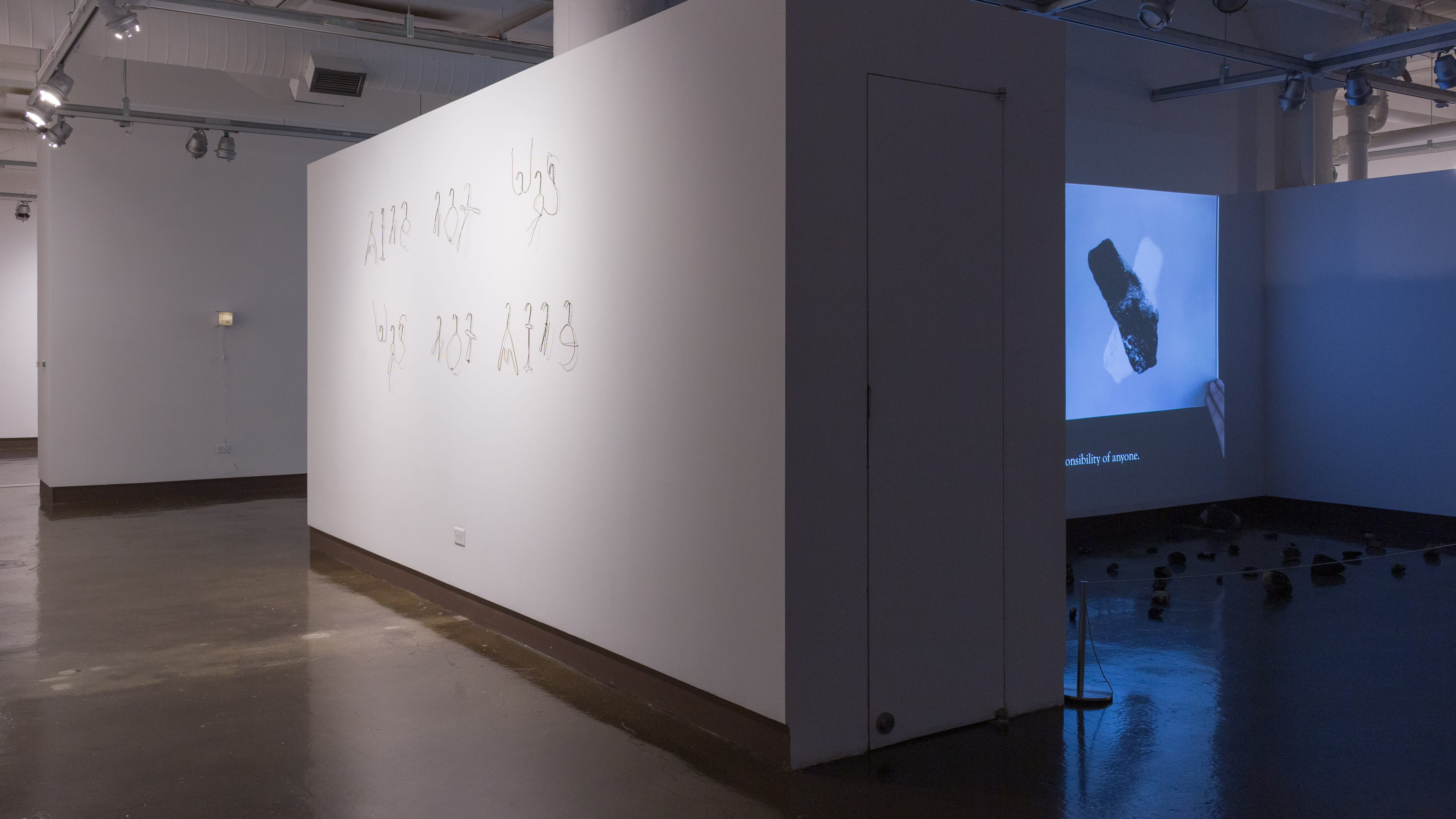 View from back corner of gallery, showing very expansive corridor to the left, and on the right is a recessed area screening a projected video.