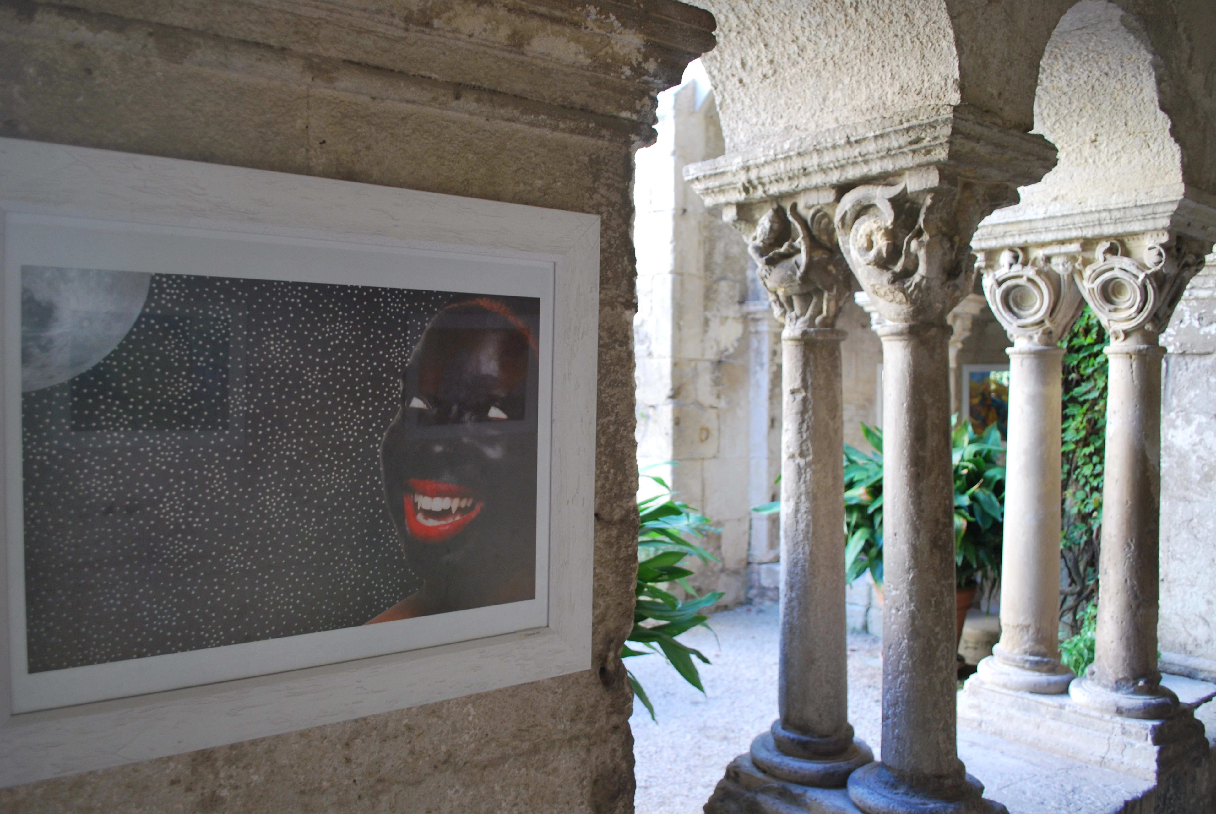 Beside a gap that looks out onto a courtyard there is a photograph of a woman smiling, looking up at the moon. Her face is painted with black paint, her lips are bright red, and she has fangs like a vampire.