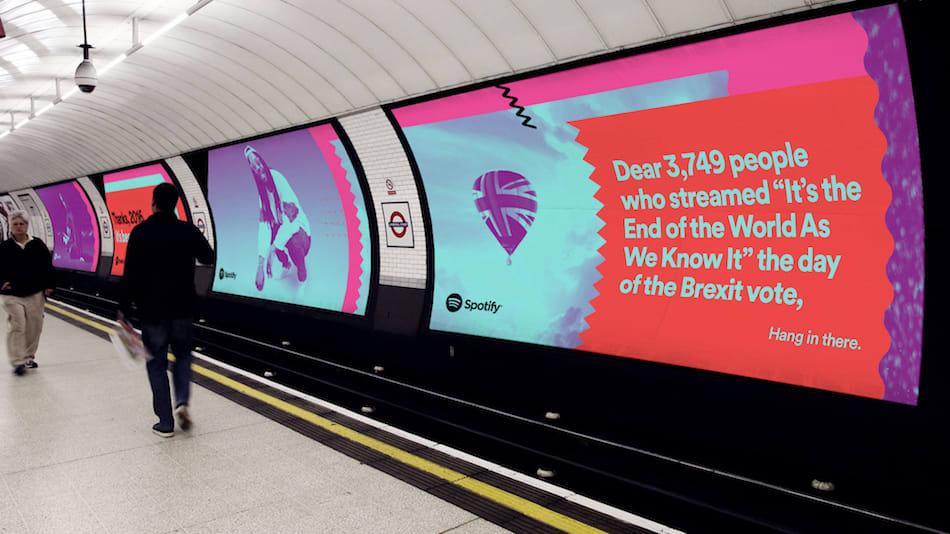 <p "="">A photograph of a London tube station with large colorful ads displayed on the wall.
