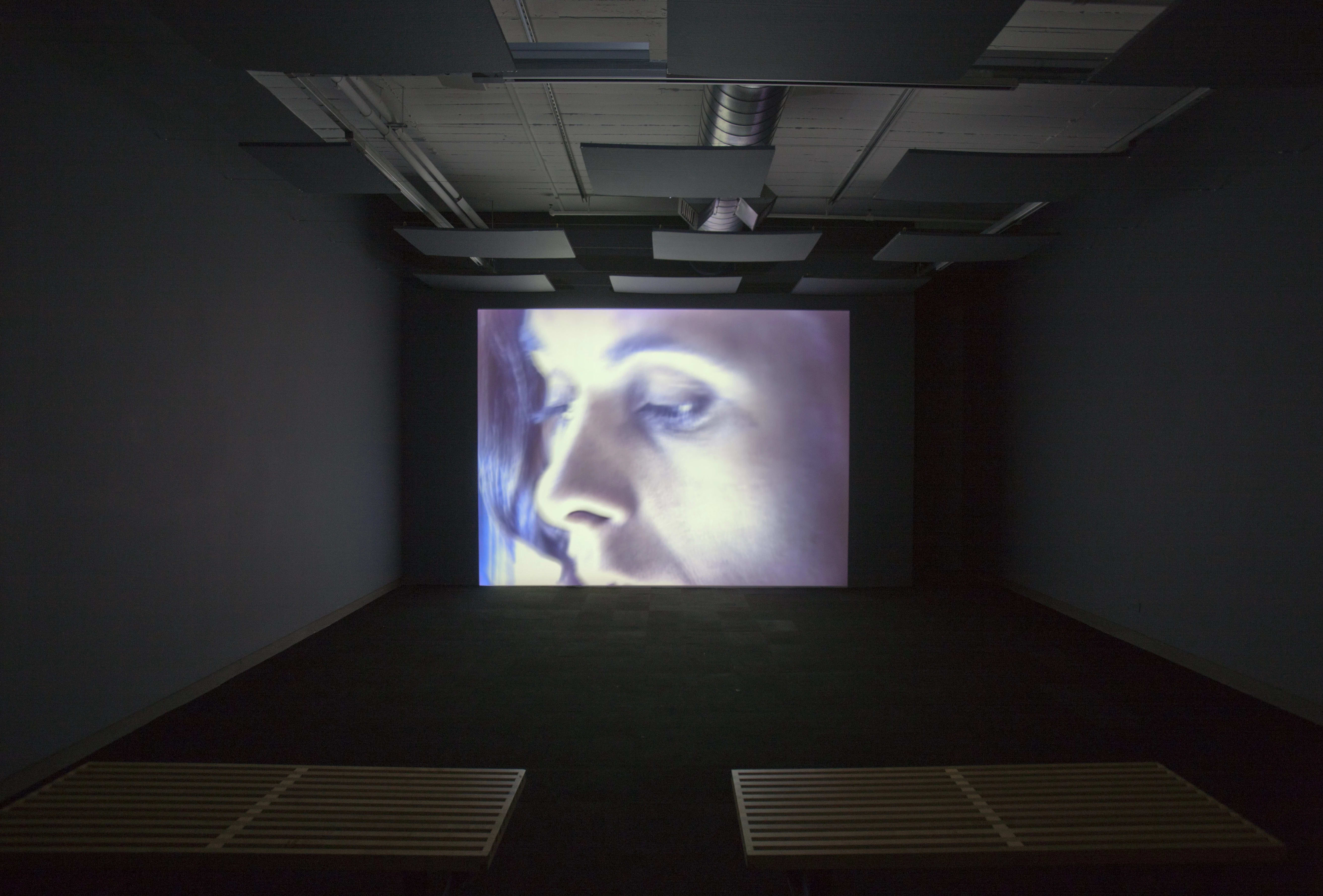 A screen in a dark room glowing with a woman's face.