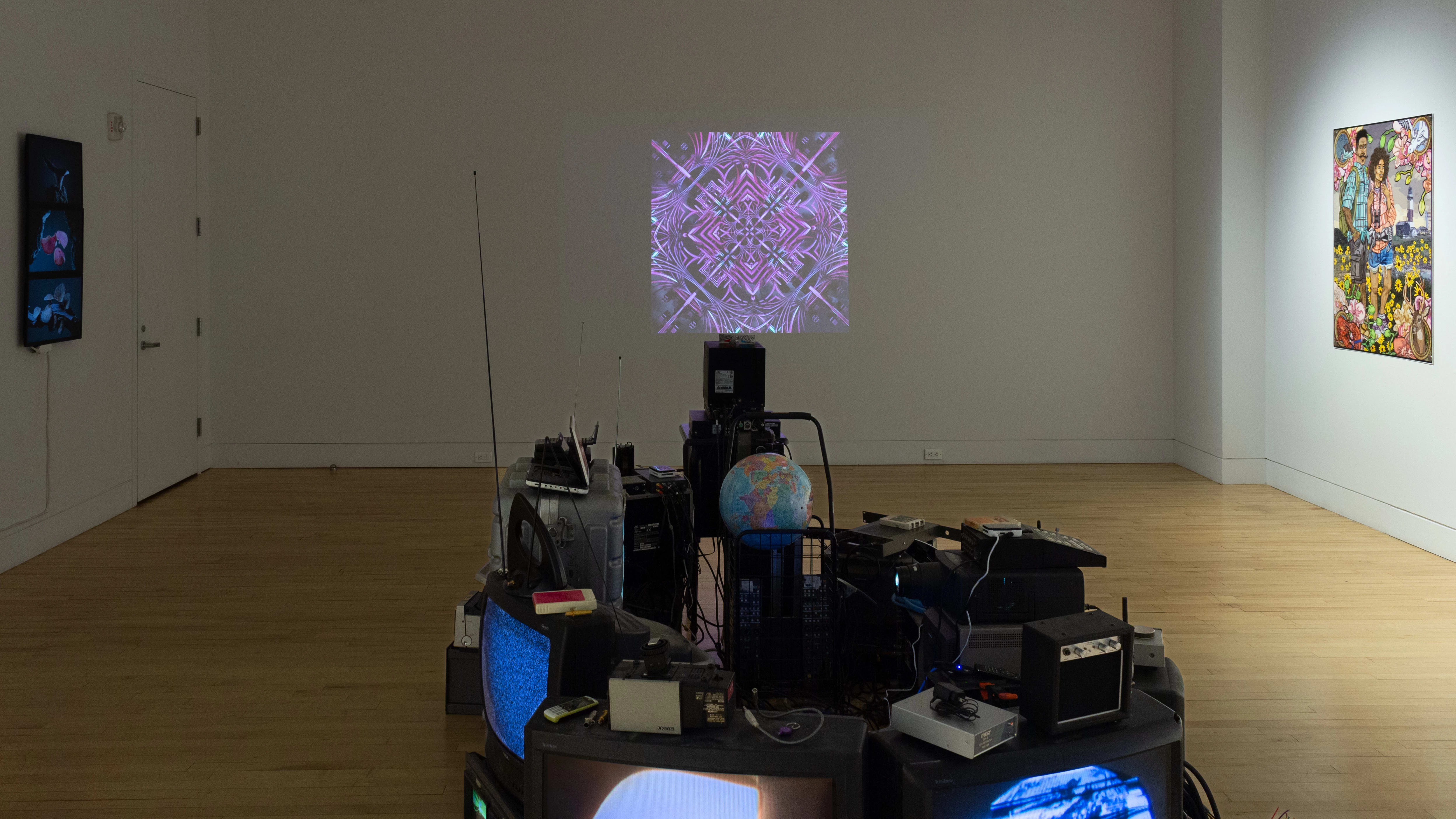 A projection of purple and blue geometric patterns plays on a wall straight ahead, with an installation of technological equipment and a globe in the foreground.