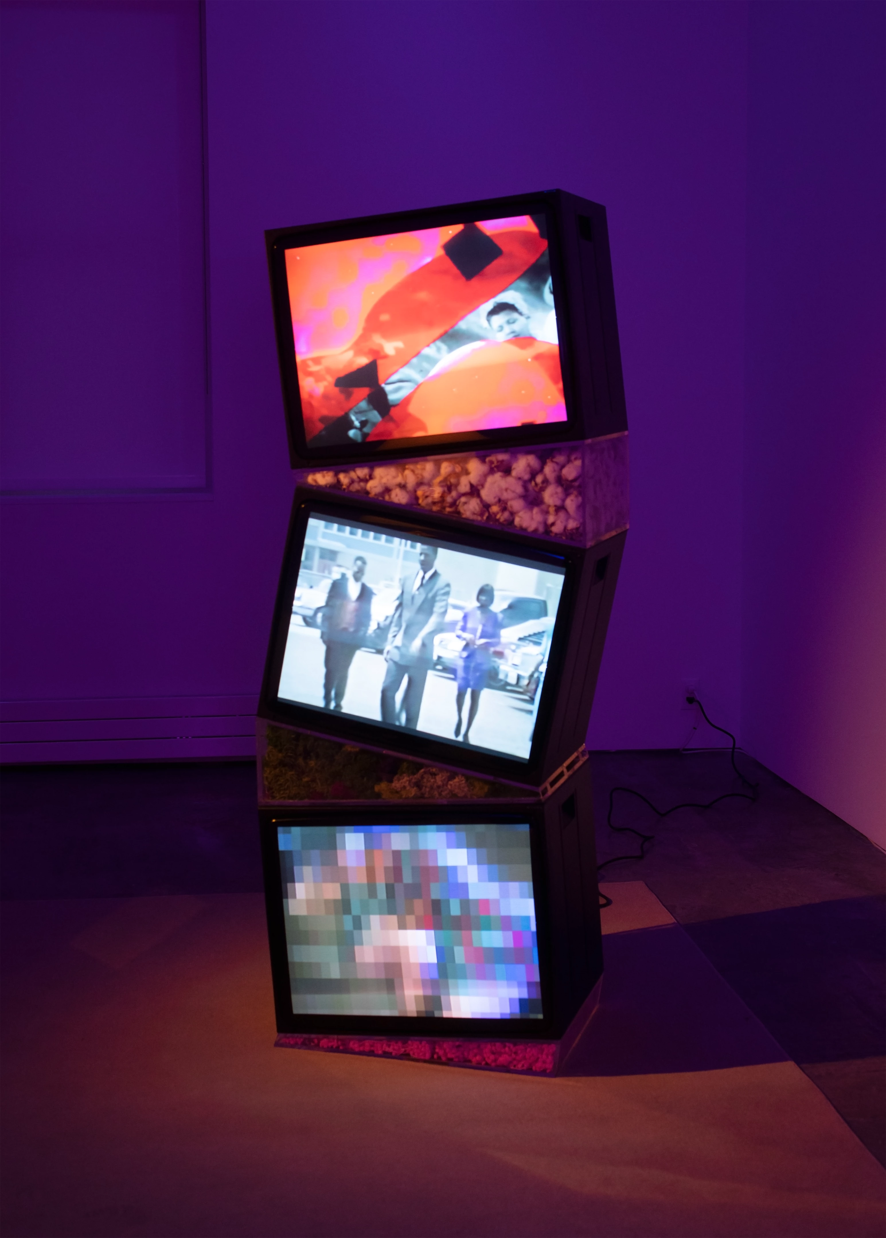 Picture of a museum installation with three old televisions stacked on top of each other, with different videos playing on each of them.