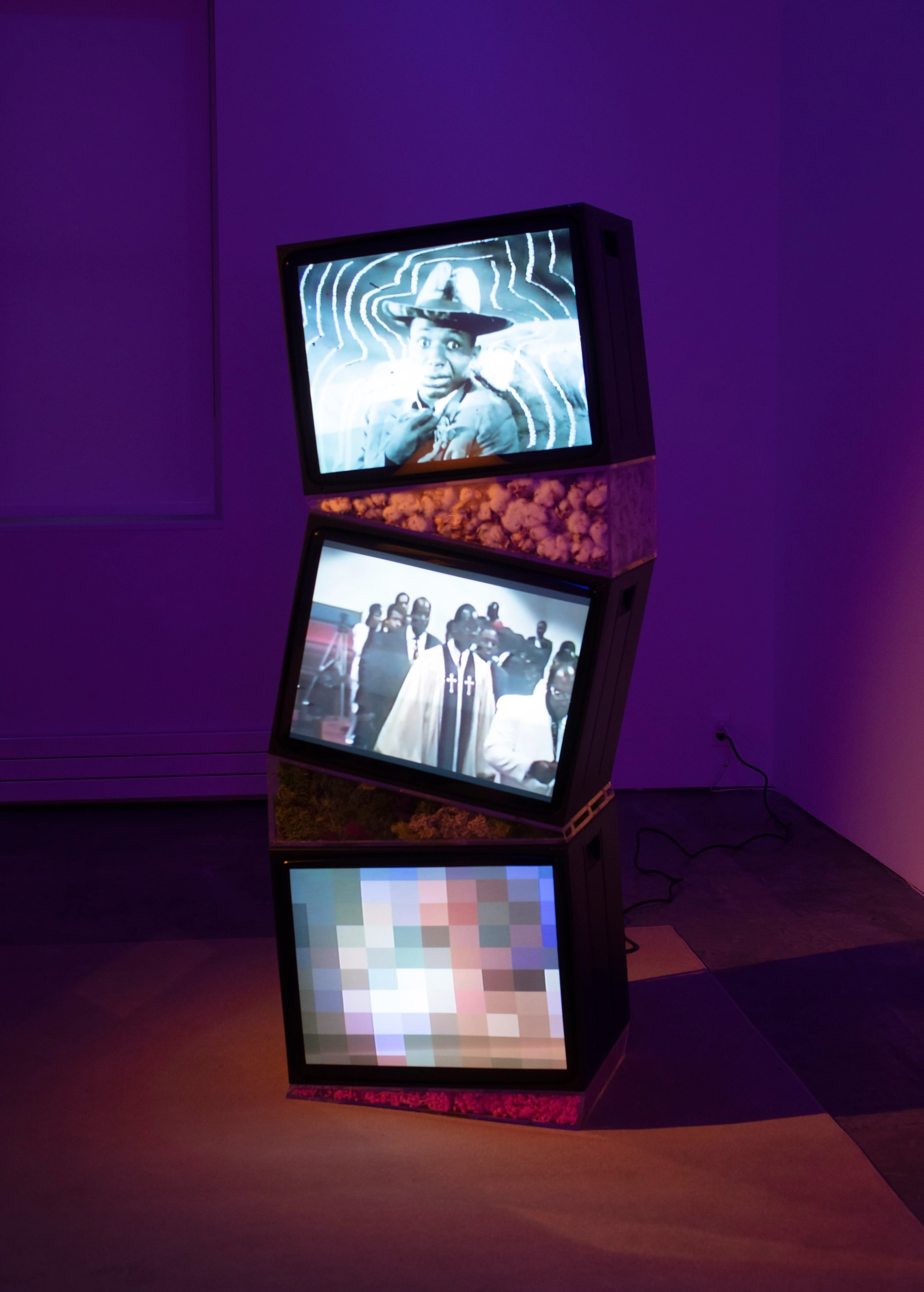 Picture of a museum installation with three old televisions stacked on top of each other, with different videos playing on each of them.