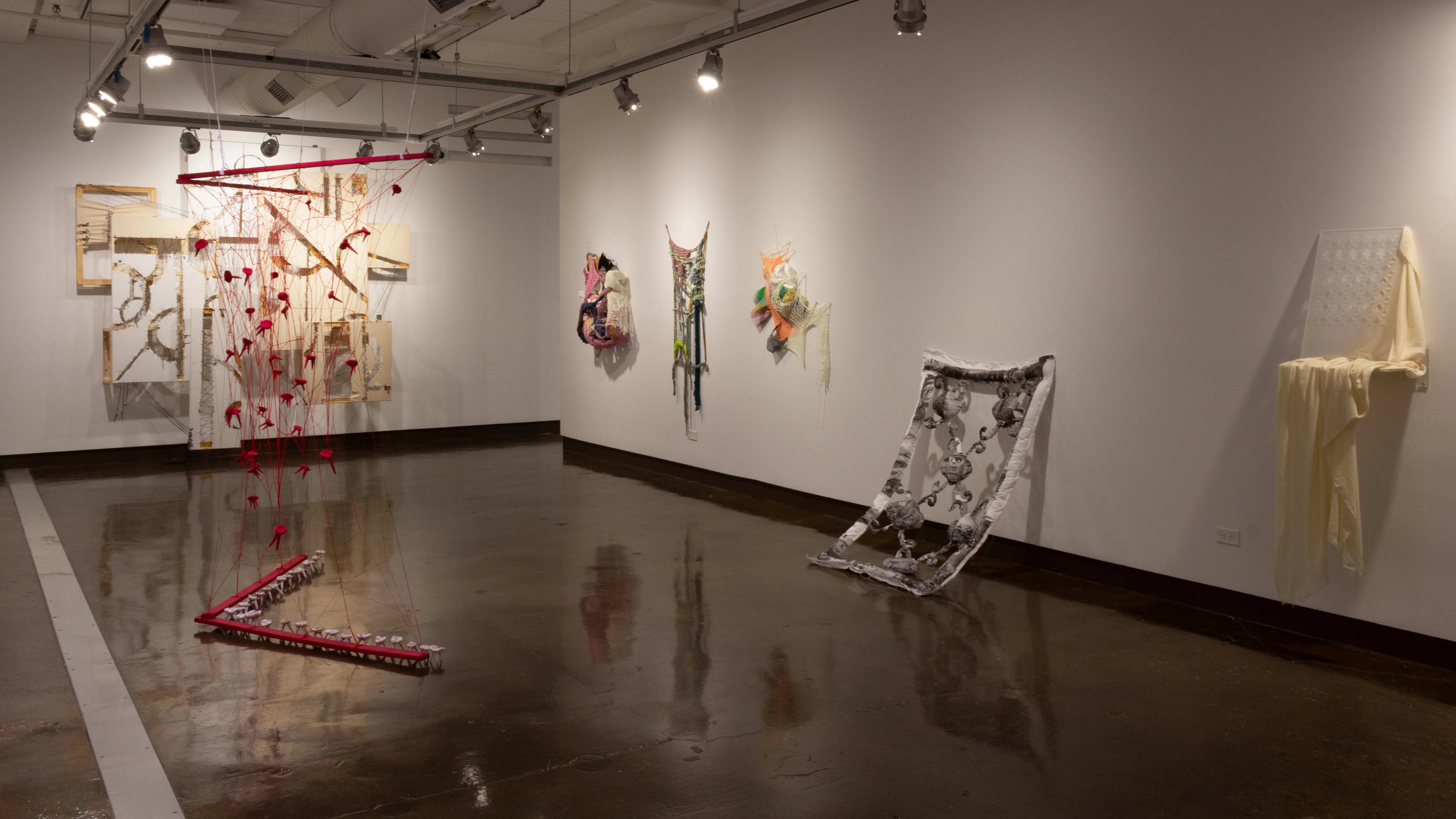 Installation view featuring several mixed media installations on the walls and a large red framed sculpture on the floor.