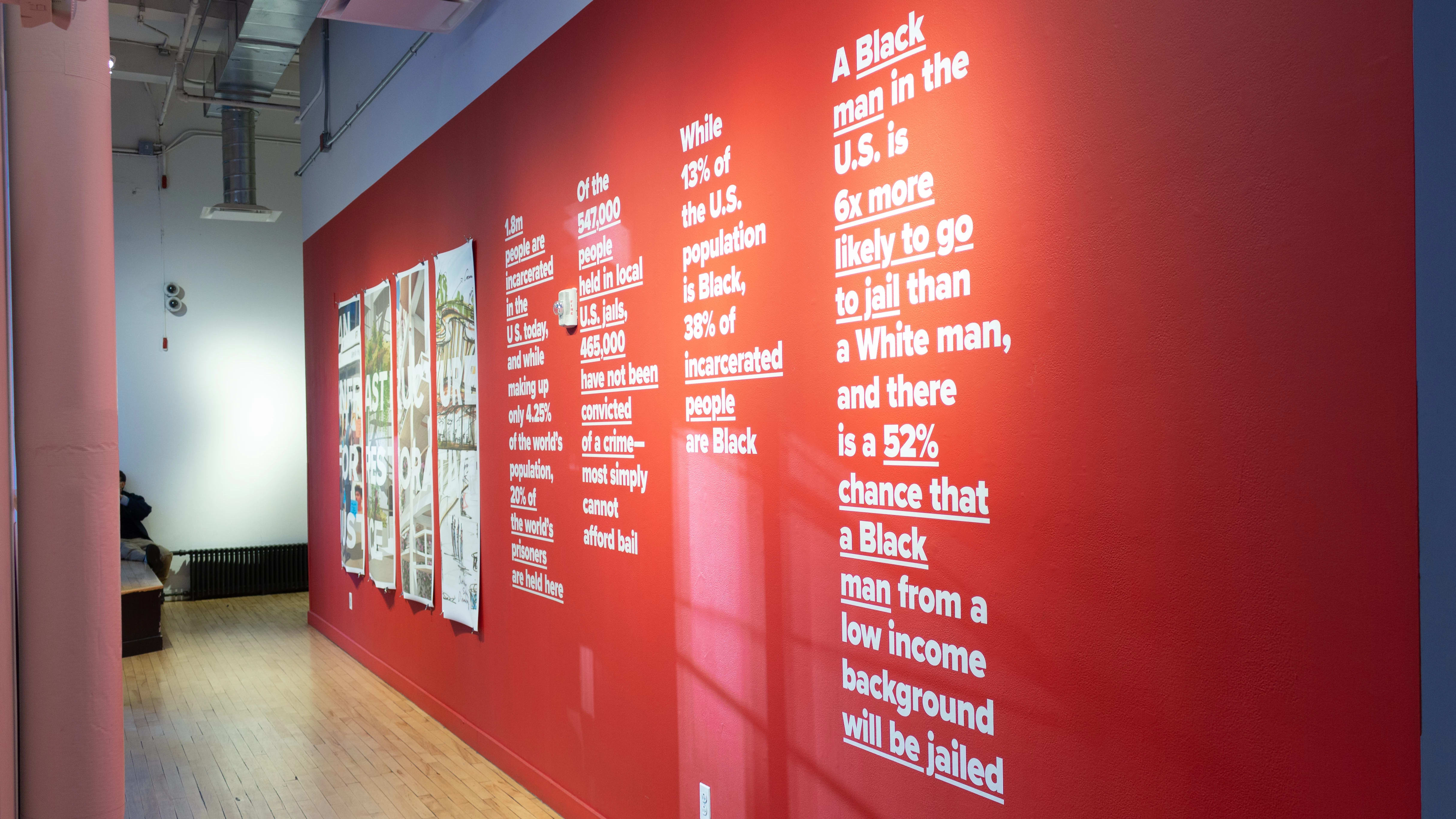 Exhibition view of An Infrastructure for Restorative Justice, featuring hallway painted red with a large posters and text on the wall.