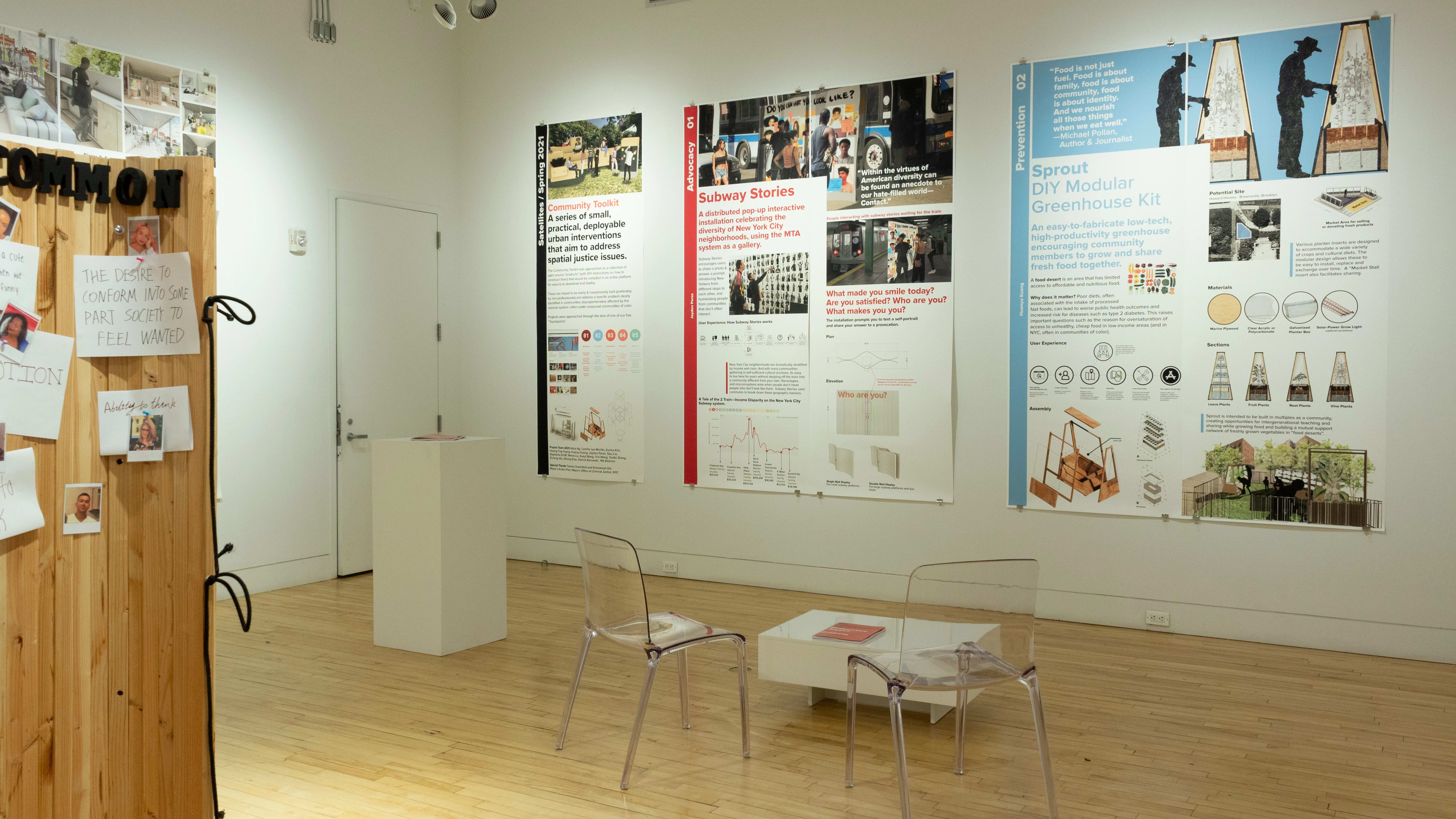Exhibition view of An Infrastructure for Restorative Justice, featuring wooden sculpture, table, 2 clear chairs, and large posters on the walls.