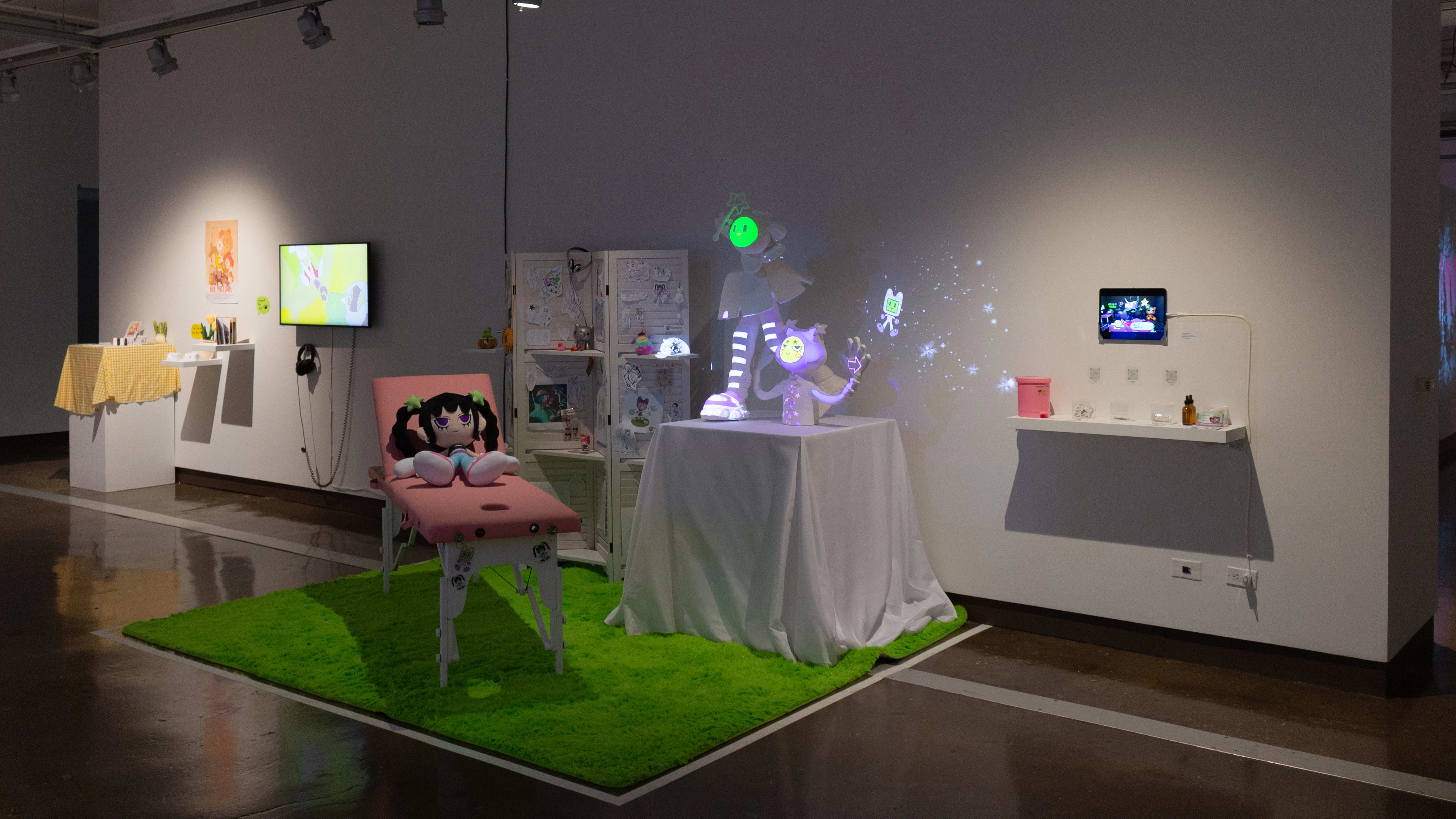 Installation image featuring a large multi-media installation with a green rug, pink doctor table and map projection on figurative sculptures on a table.