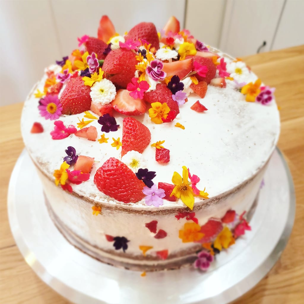A photograph of a white-frosted cake decorated with flower petals and strawberries.