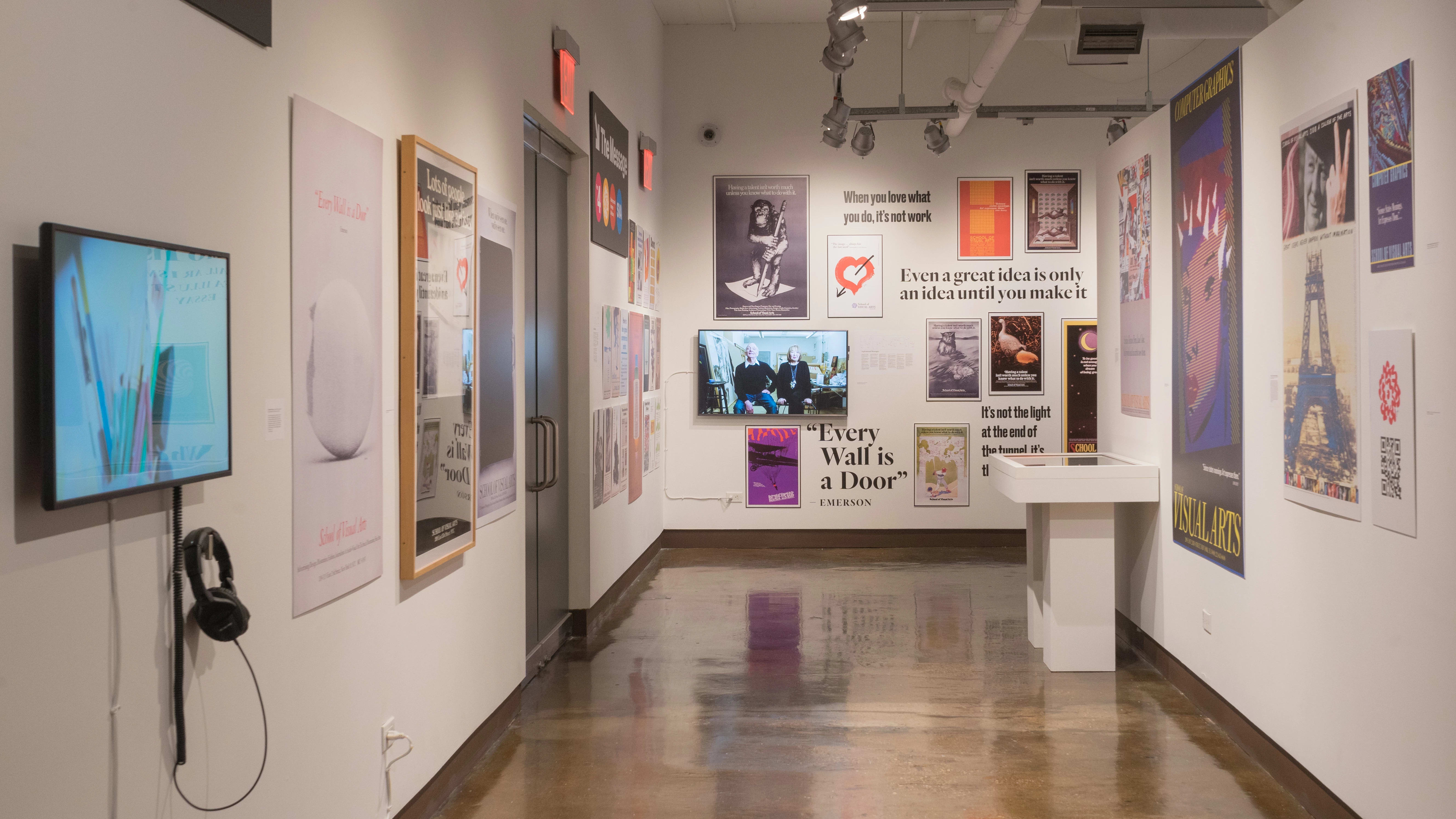 Posters of varying sizes hang across two walls in a gallery space along with pull quotes and a video screen.