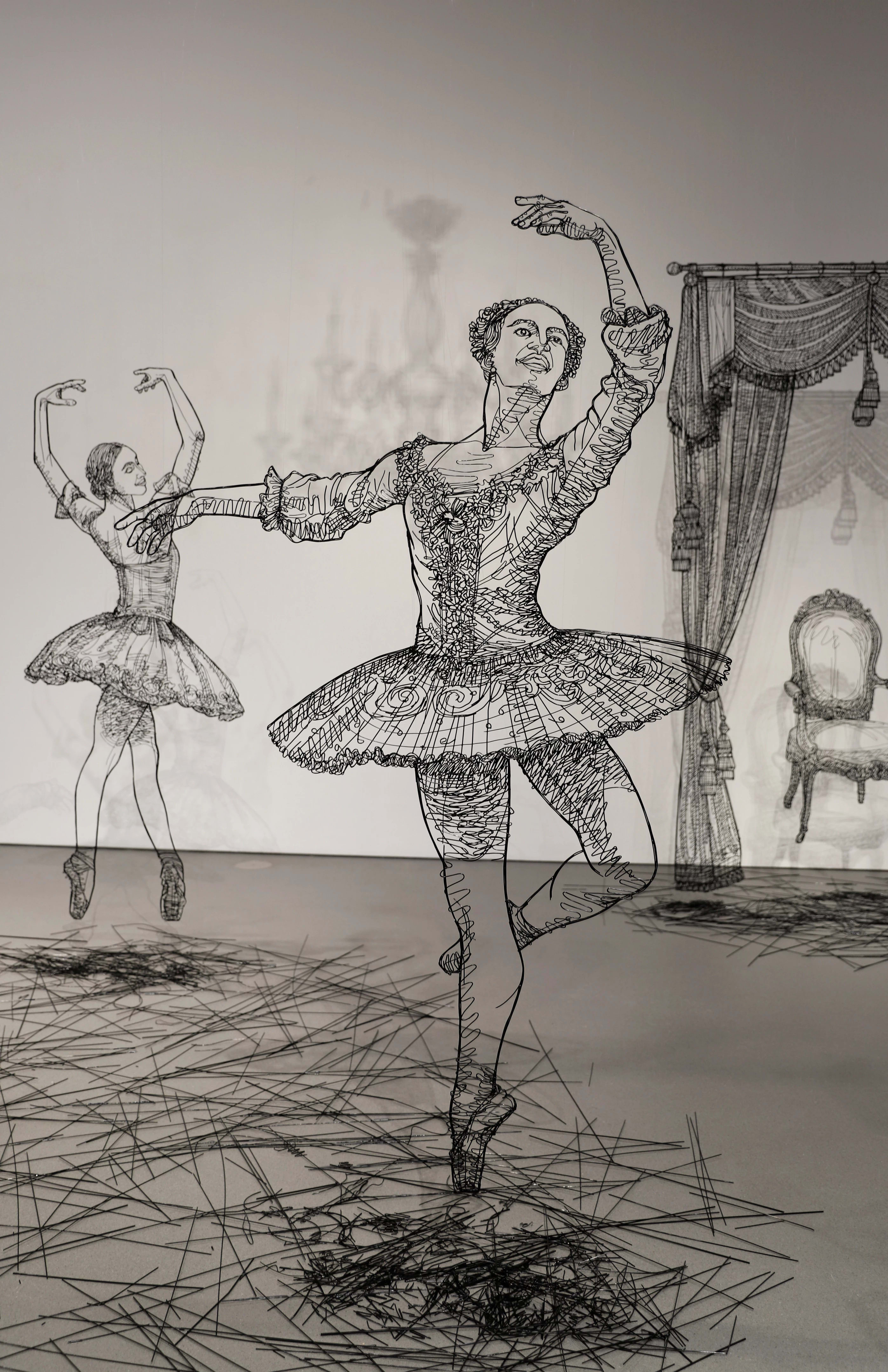 Close up of sculptures made in black wire of several large scale ballerinas dancing around a white room.