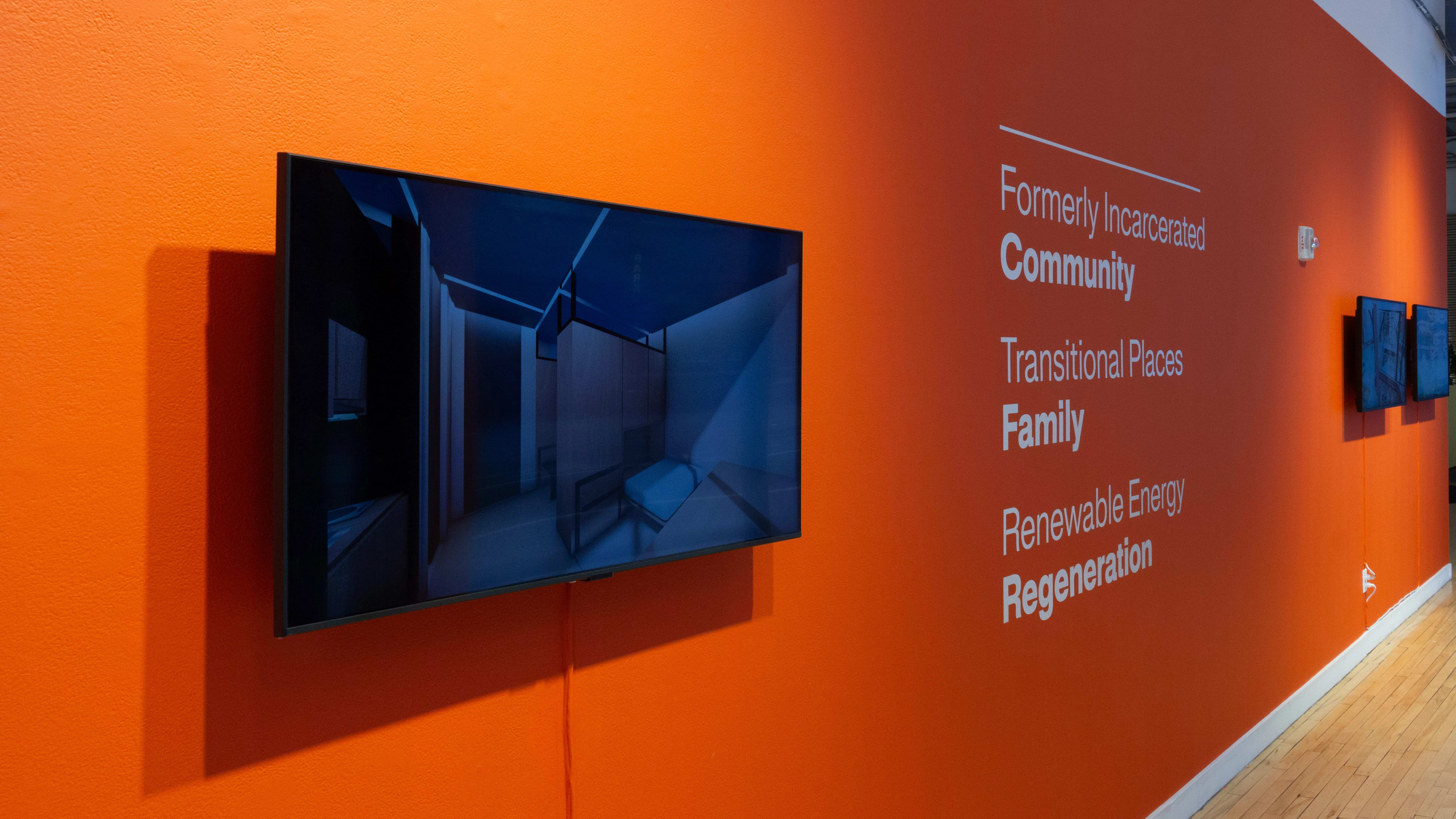 Installation image of an angled view of an orange wall with text and three monitors.