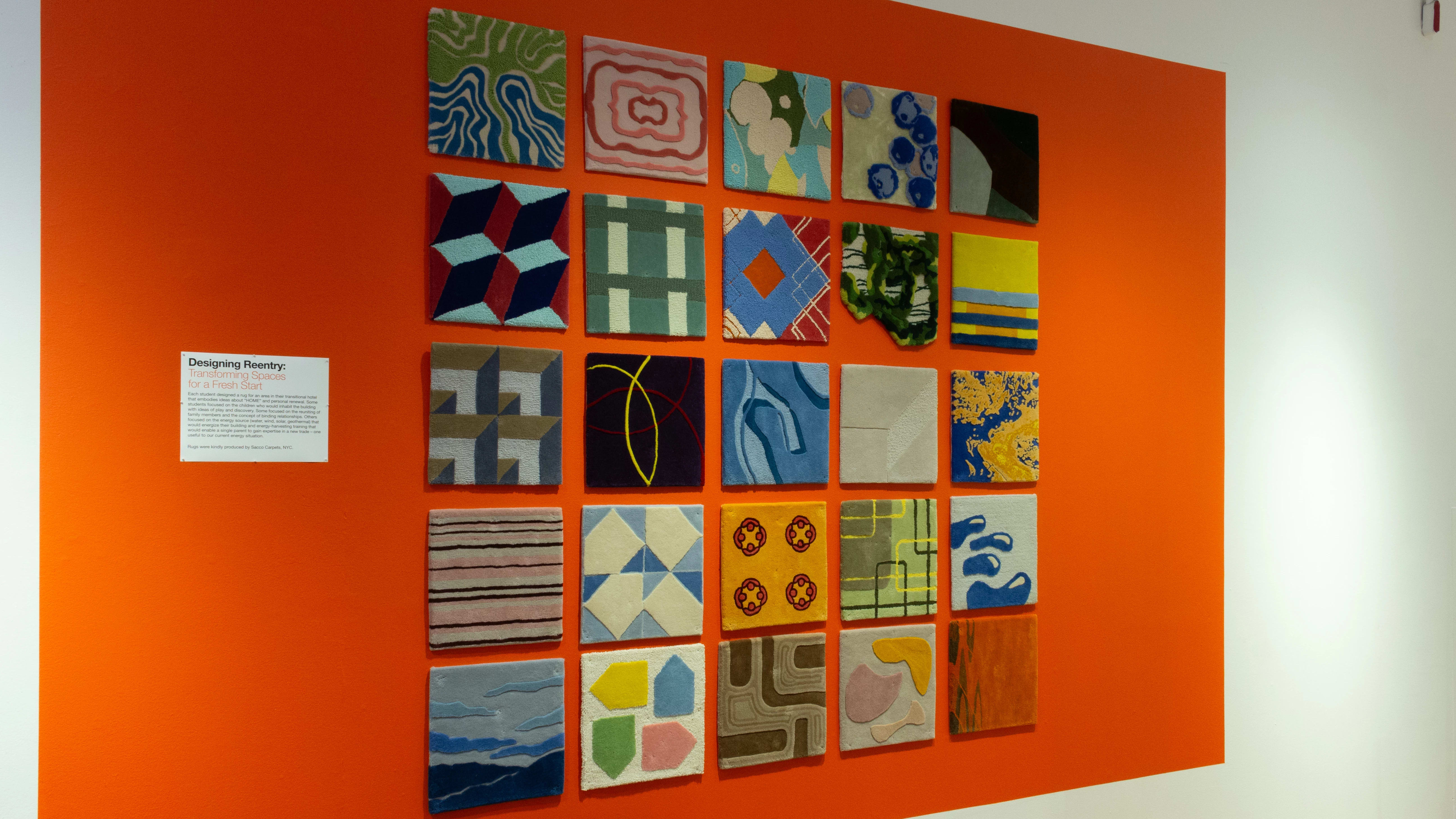 Installation image of an angled view of an orange wall with carpet squares of differing patterns.