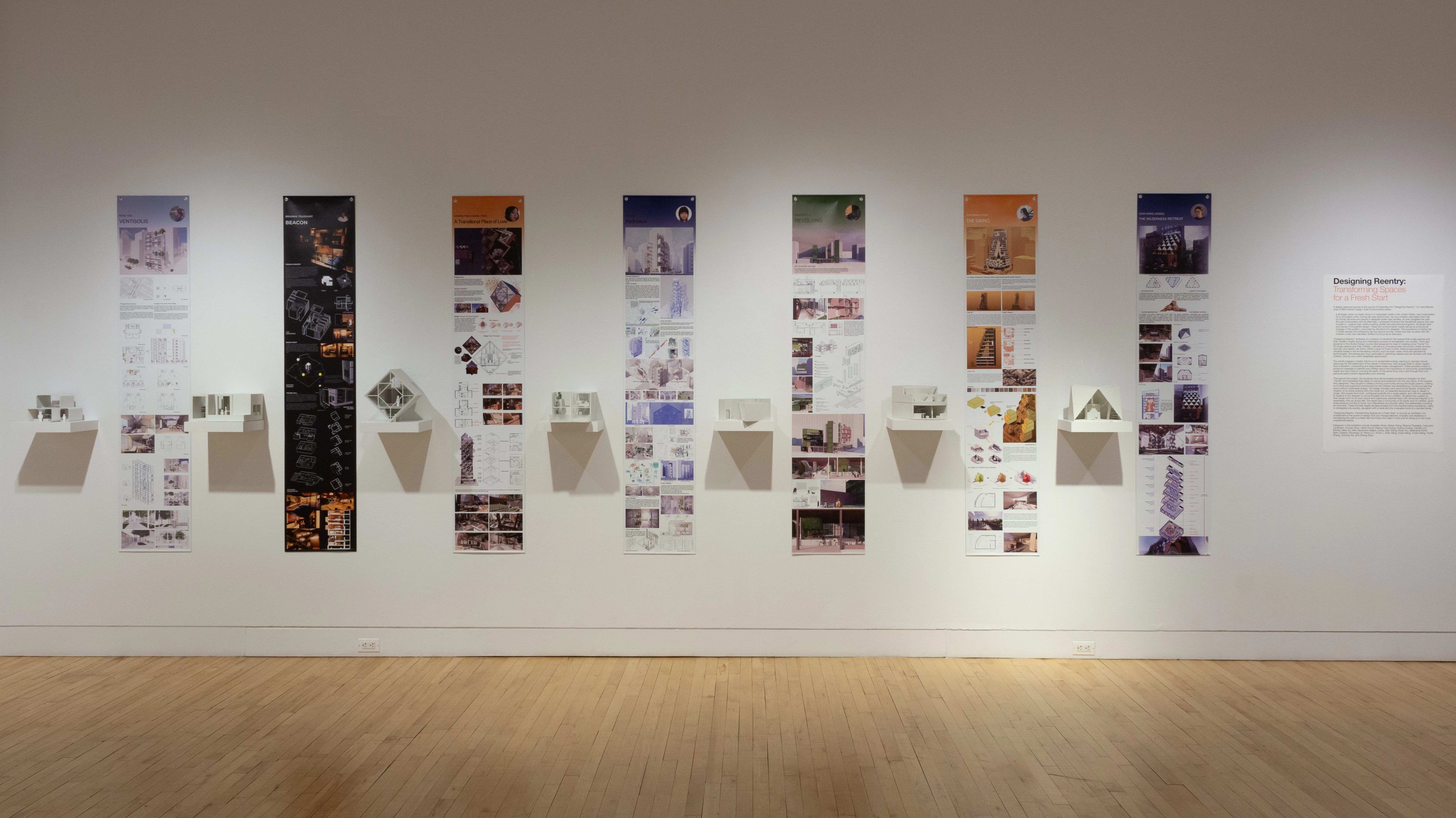 Installation image showing a straight view of a gallery wall with seven building models on shelves, and information banners for each to the right.