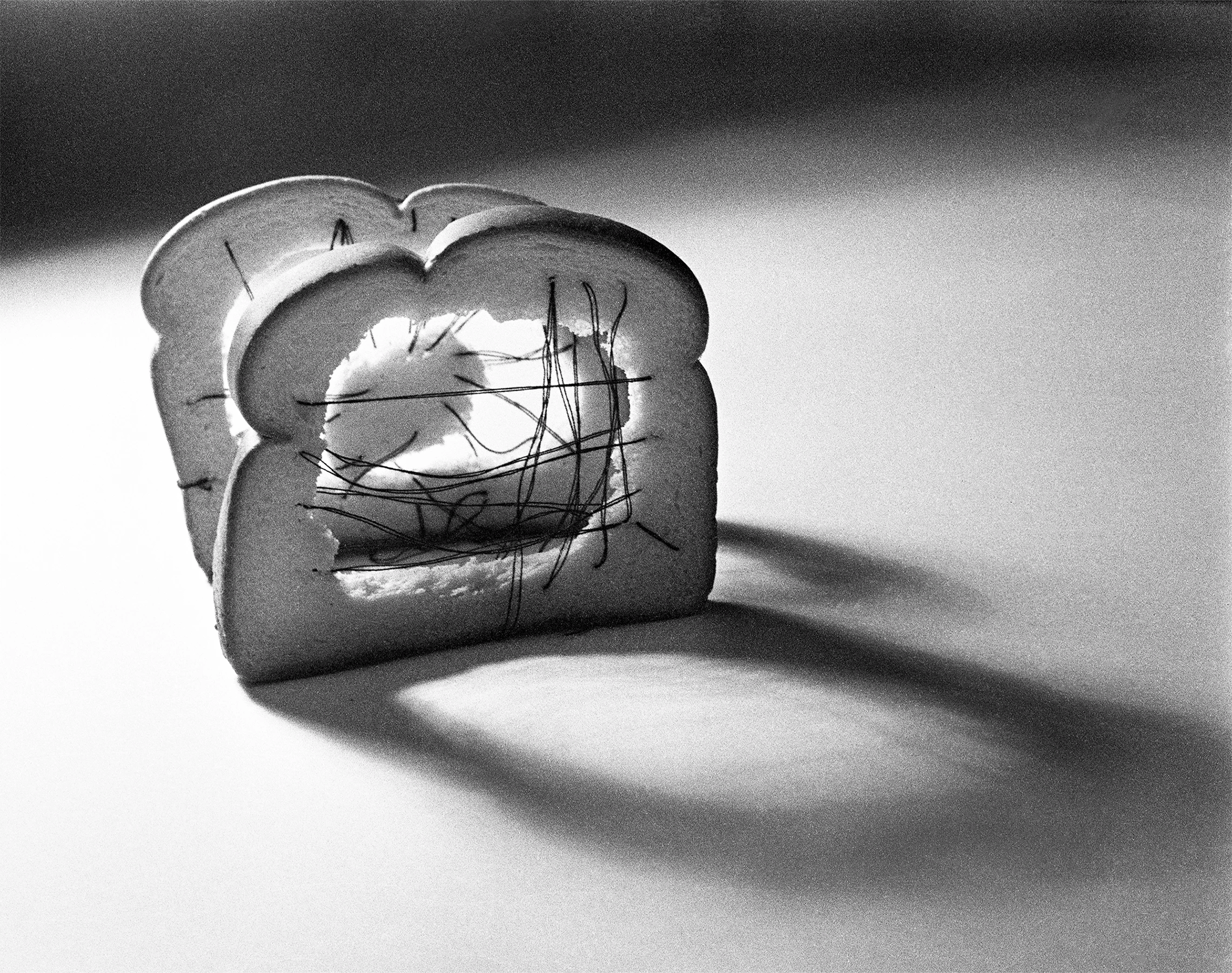 A black and white photo of two slices of bread sewn with thread.