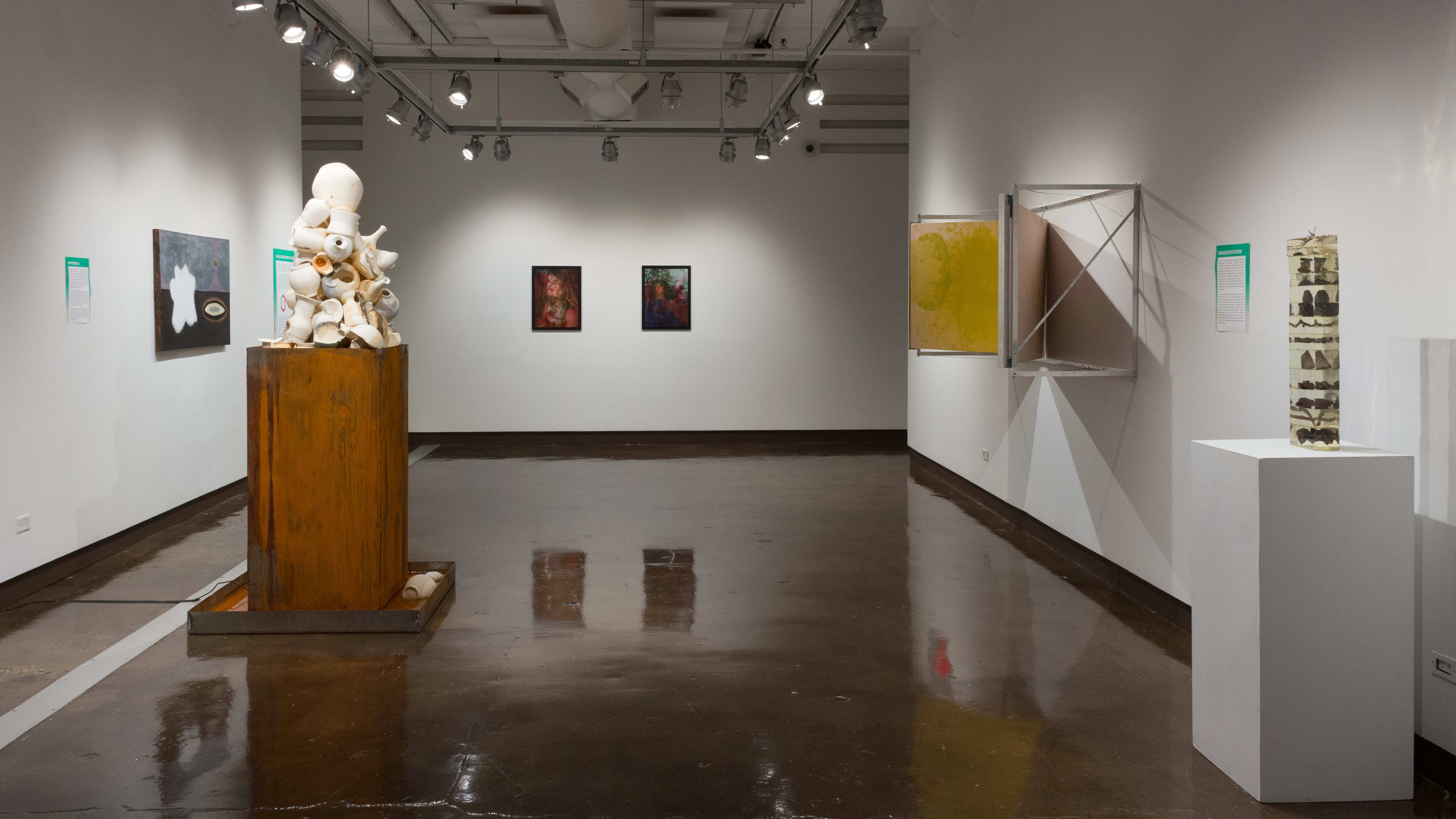 From the opposite side of the space, two prints of photographs are visible on a far wall. There are also paintings, posters, and a sculpture made of resin in the gallery.