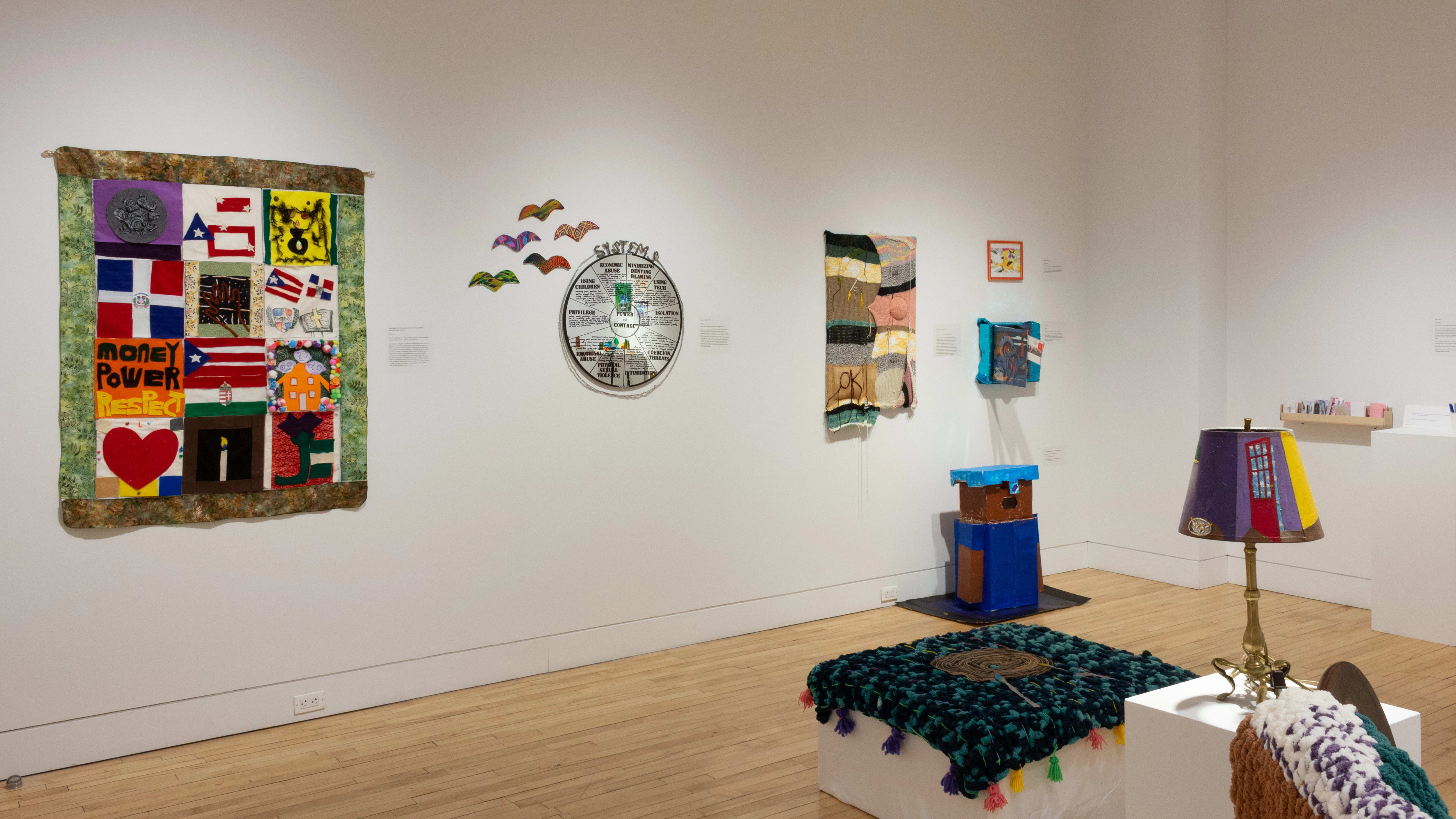 On another wall there are textile and multimedia pieces, with domestic items like an ottoman and lamp in the center of the room.