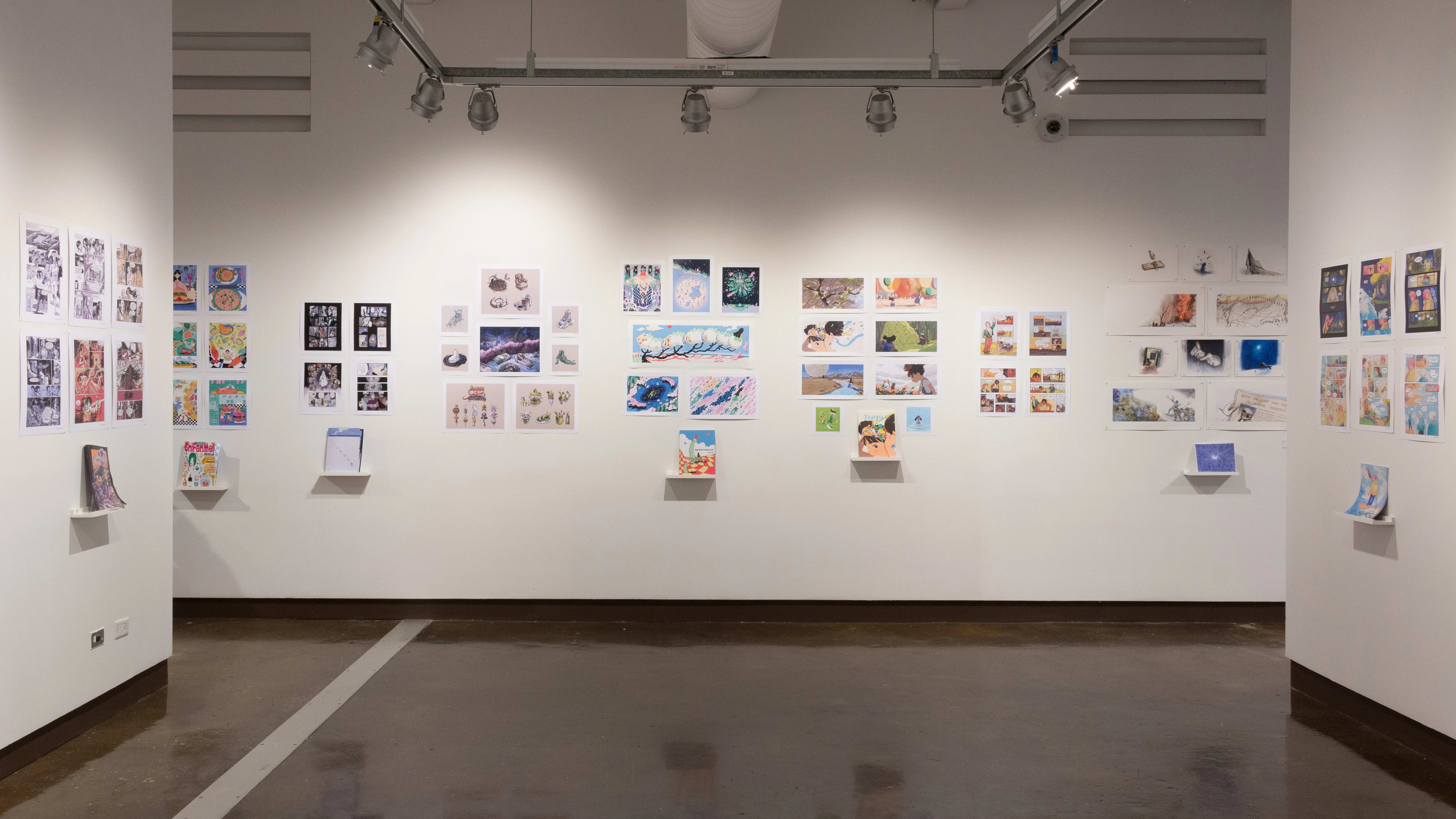 Students’ illustrated books are displayed on shelves, with prints from the books hanging on the wall above.