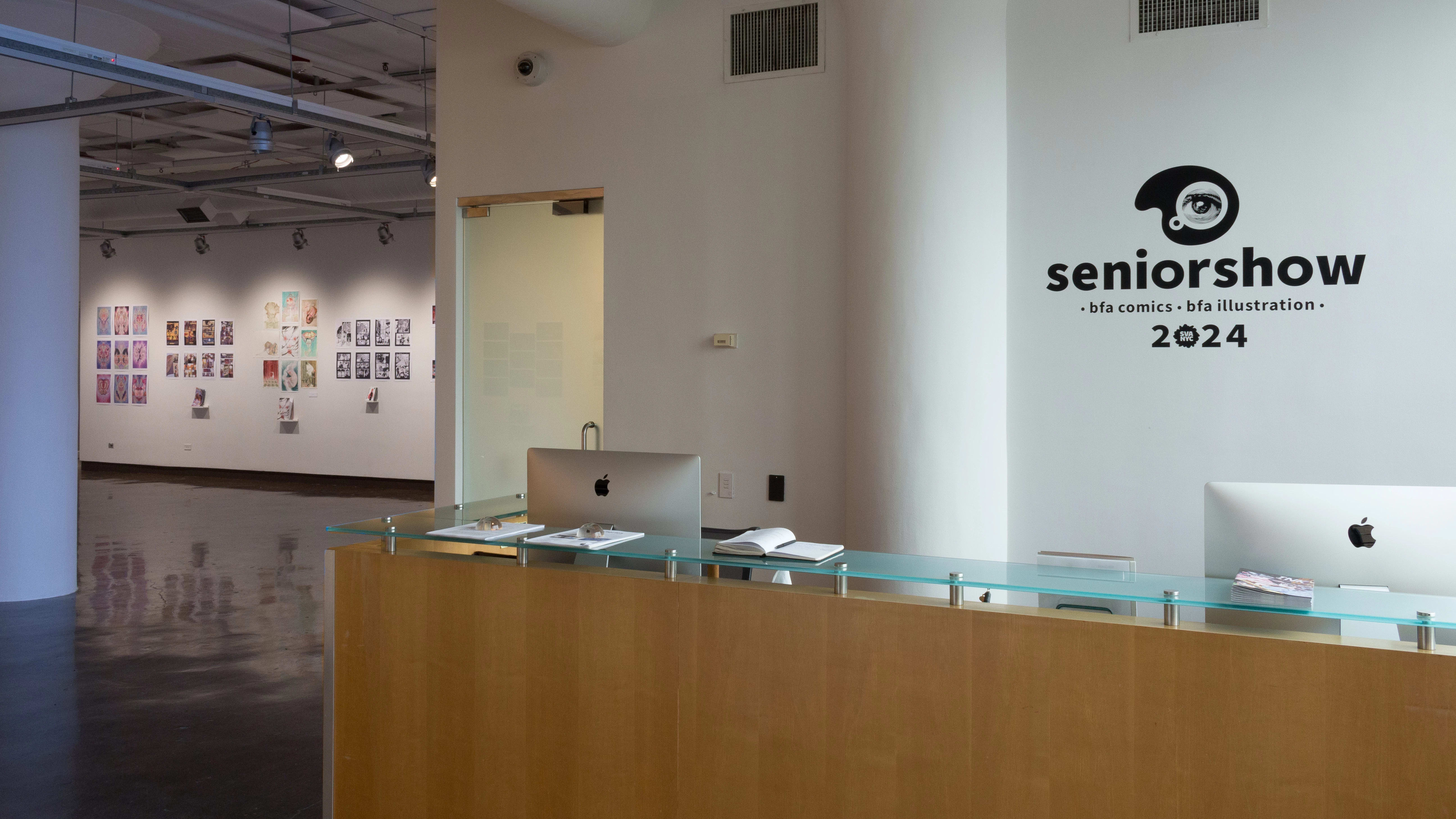 Wall vinyl for the BFA Comics / BFA Illustration Senior Show is displayed on a wall over the reception desk at the SVA Chelsea Gallery. Past the desk, work is visible on the walls of the gallery.