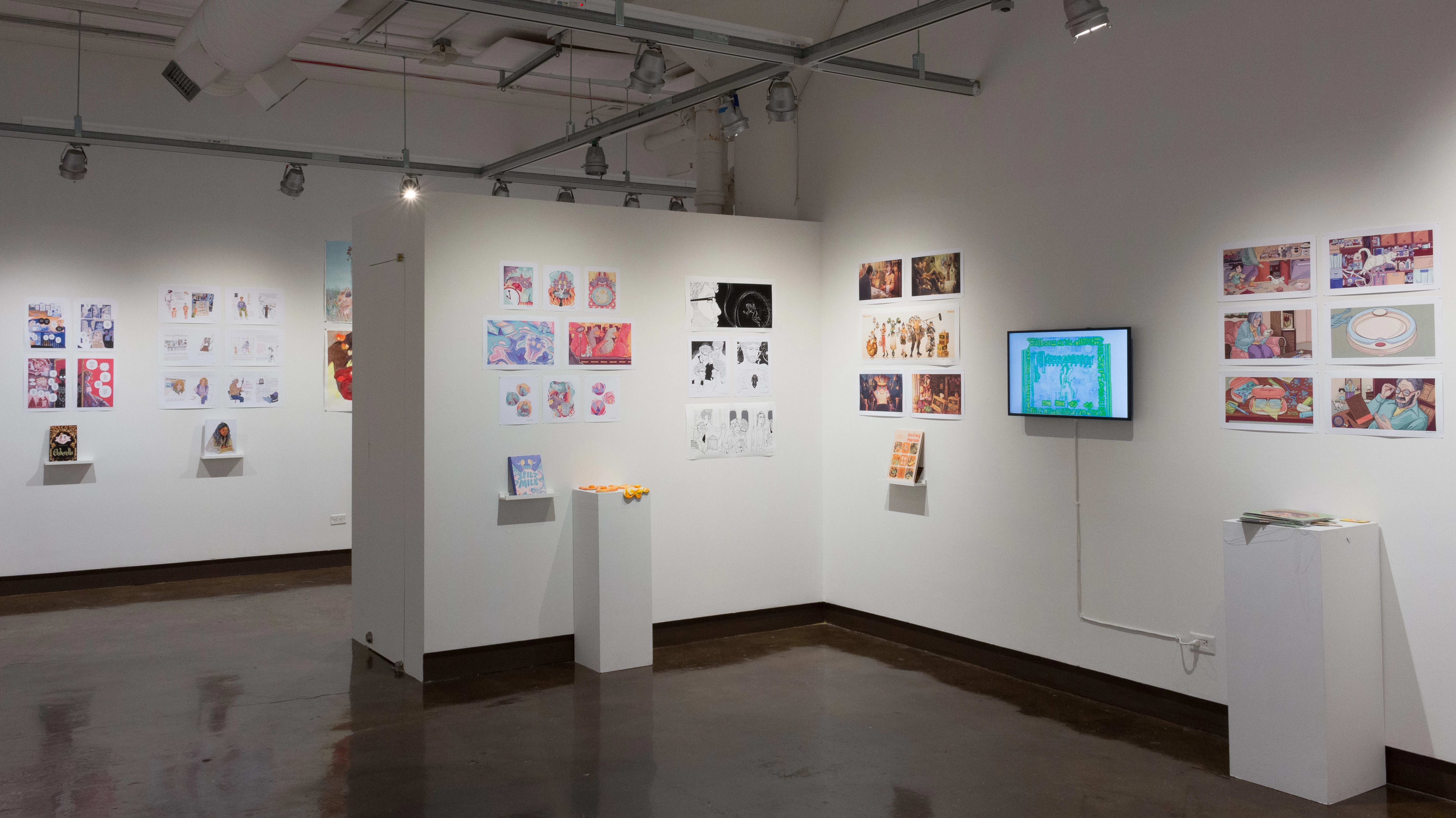 In the third gallery space, the prints hanging on the walls vary in dimension, style, and color. Books sit on shelves beneath the prints and a TV displays online works and animations and beside the TV, a pedestal holding some ceramic sculptures of fried eggs.