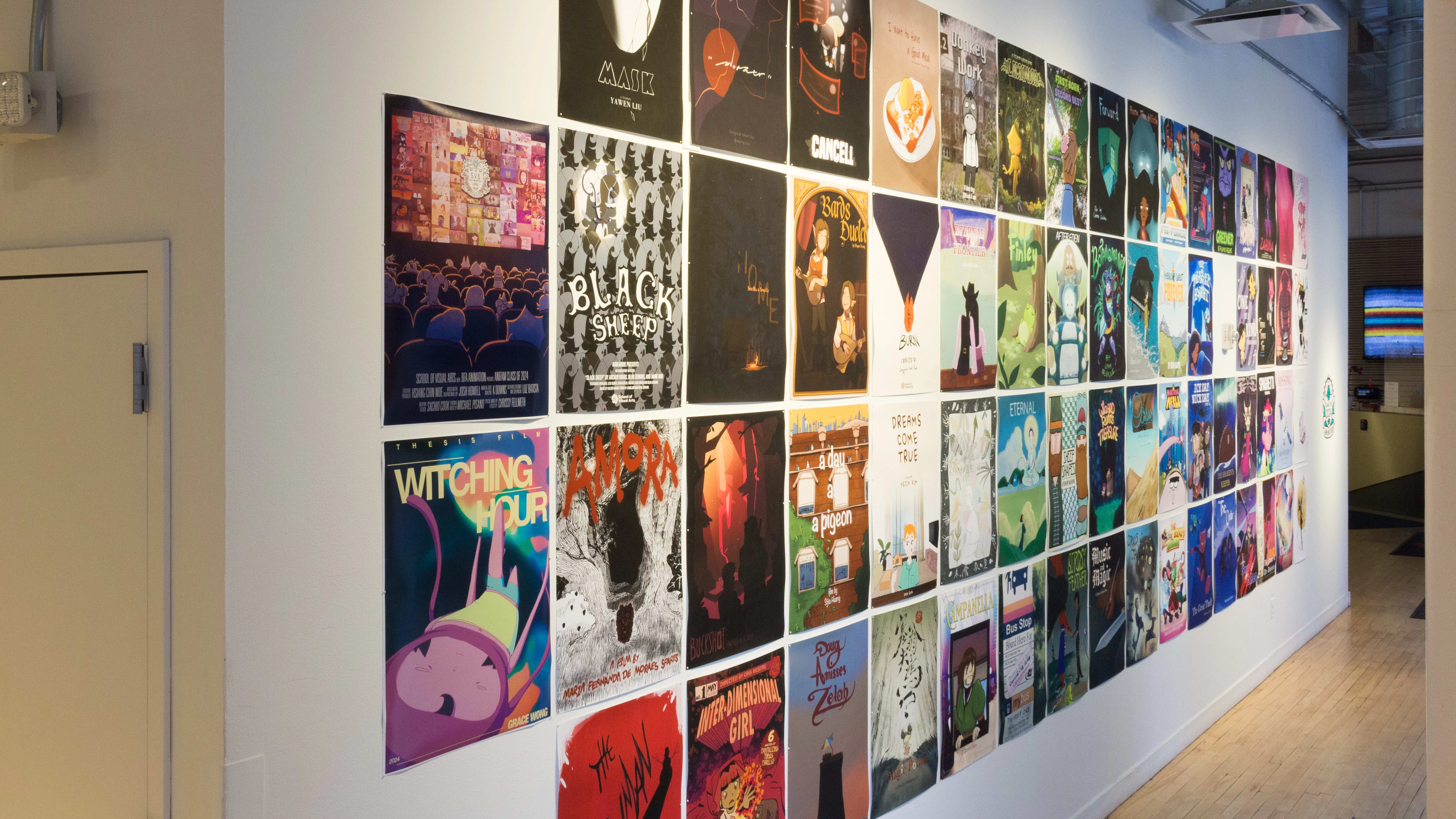 Four rows of colorful, illustrated posters are displayed in four rows on a white gallery wall. The posters are each about 11 x 14 inches.