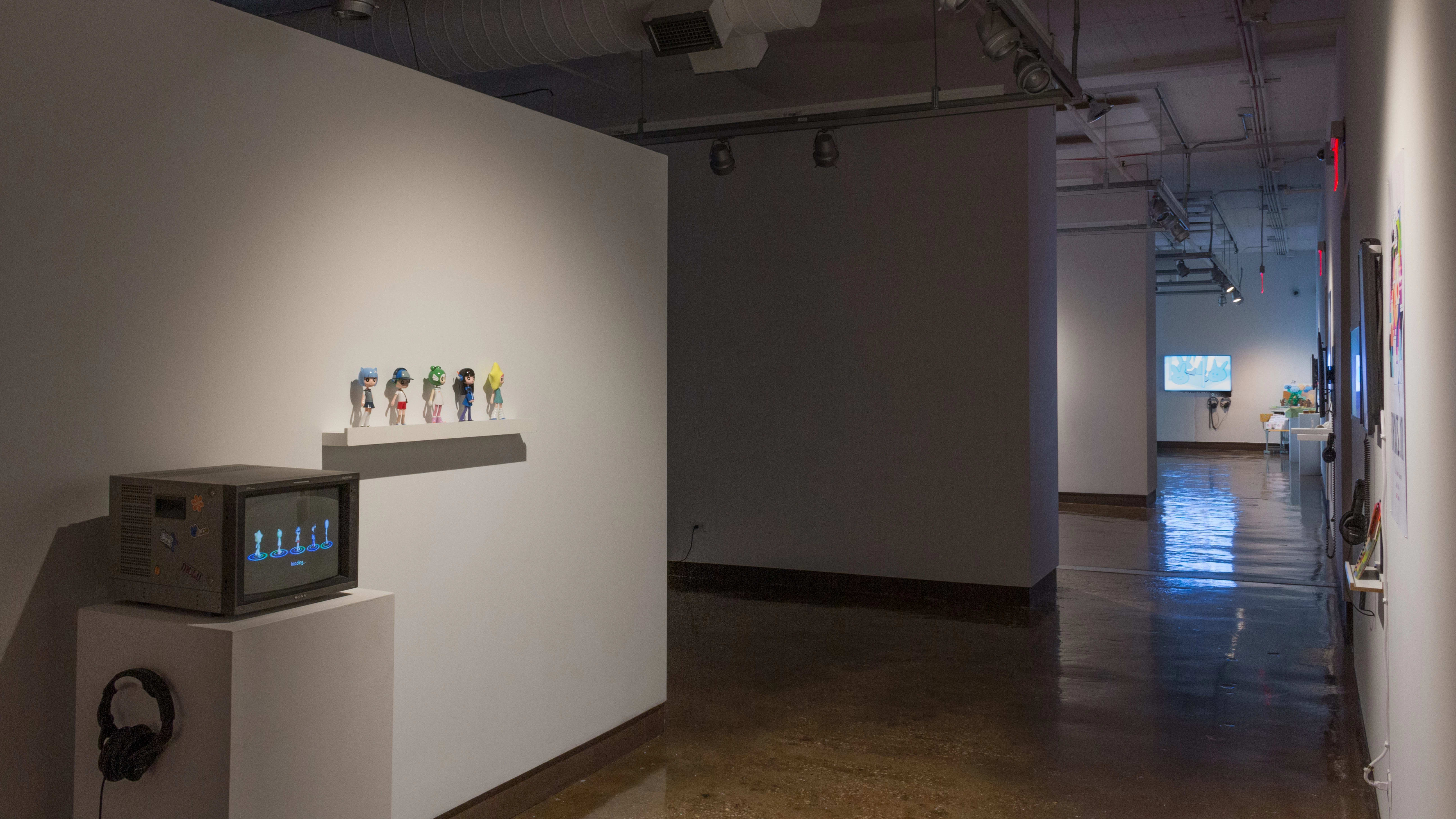 A long hallway recedes to the right of several gallery spaces, with ambient light from various projections and monitors visible in the background; an old TV is in the foreground.