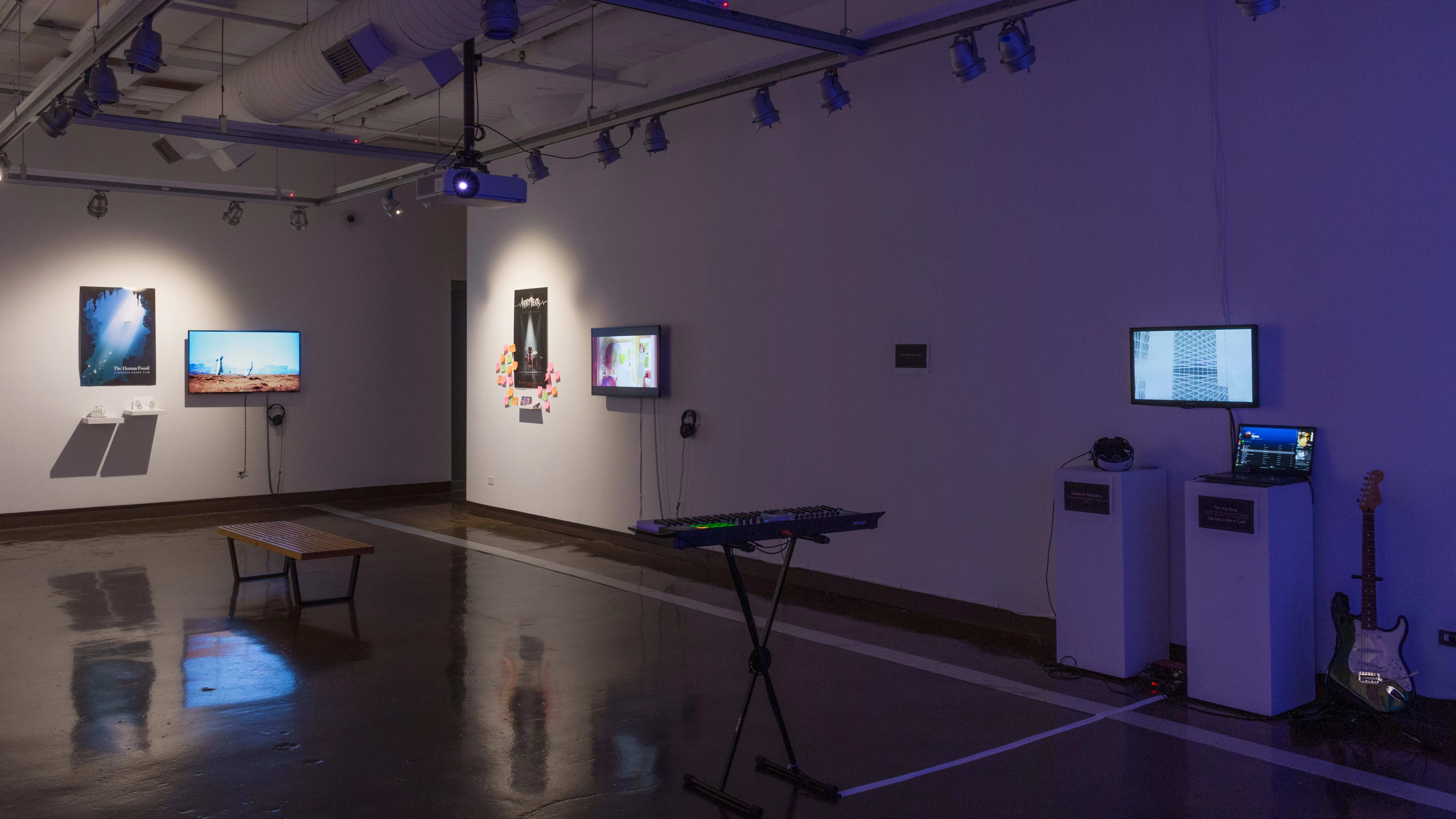 Installation image showing an angled view of a freestanding wall, with musical instruments in the foreground and several monitors and installations in the background.