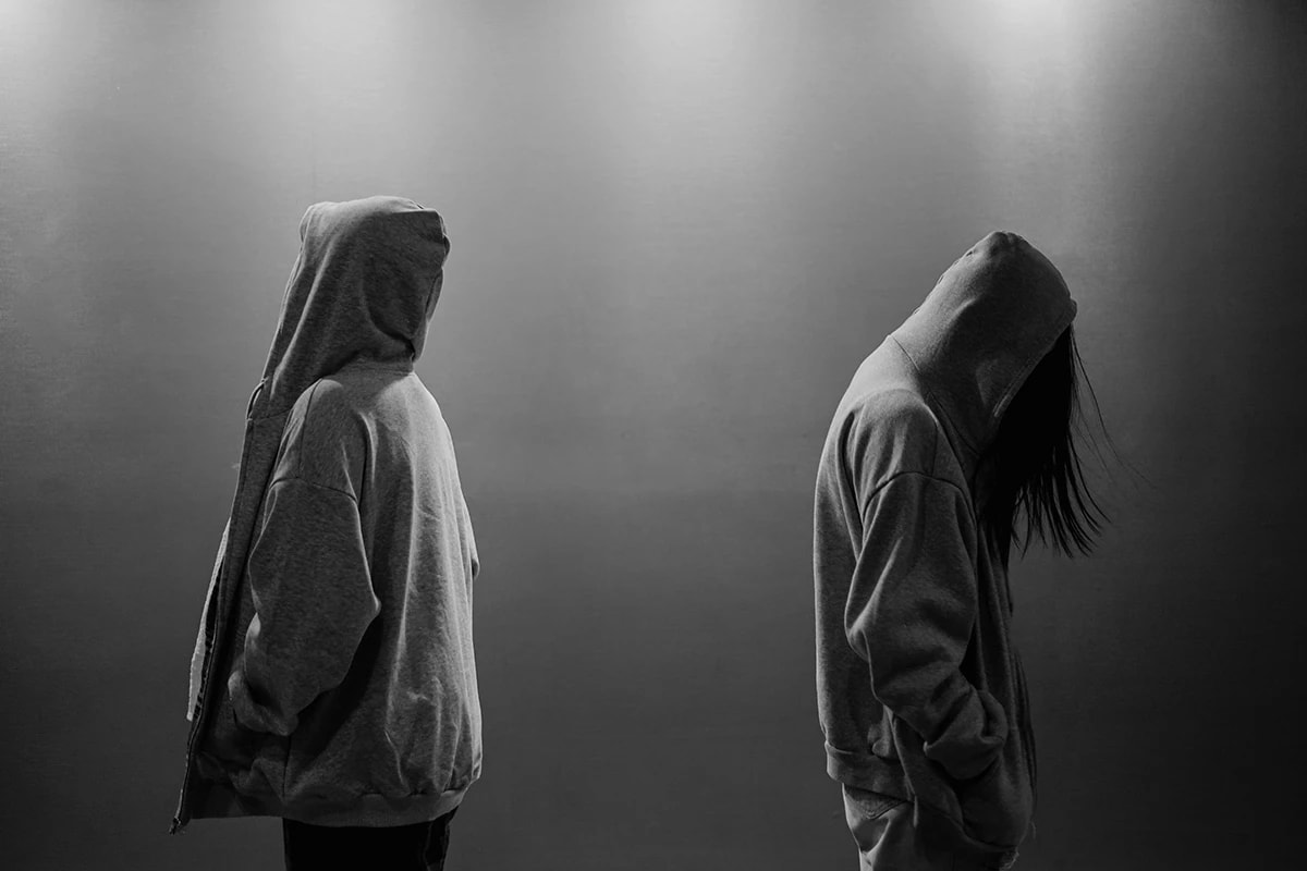 A black and white photo of two people wearing hoodies facing opposite of each other