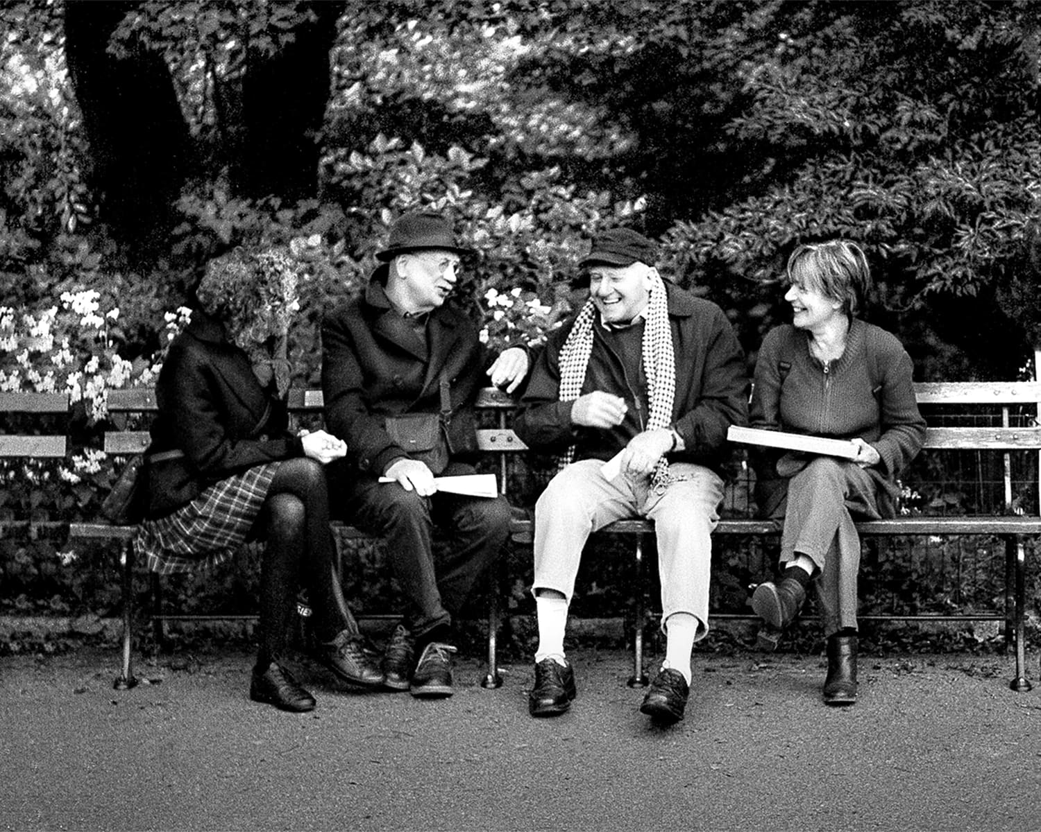 Four friends are sitting shoulder to shoulder in the park talking.