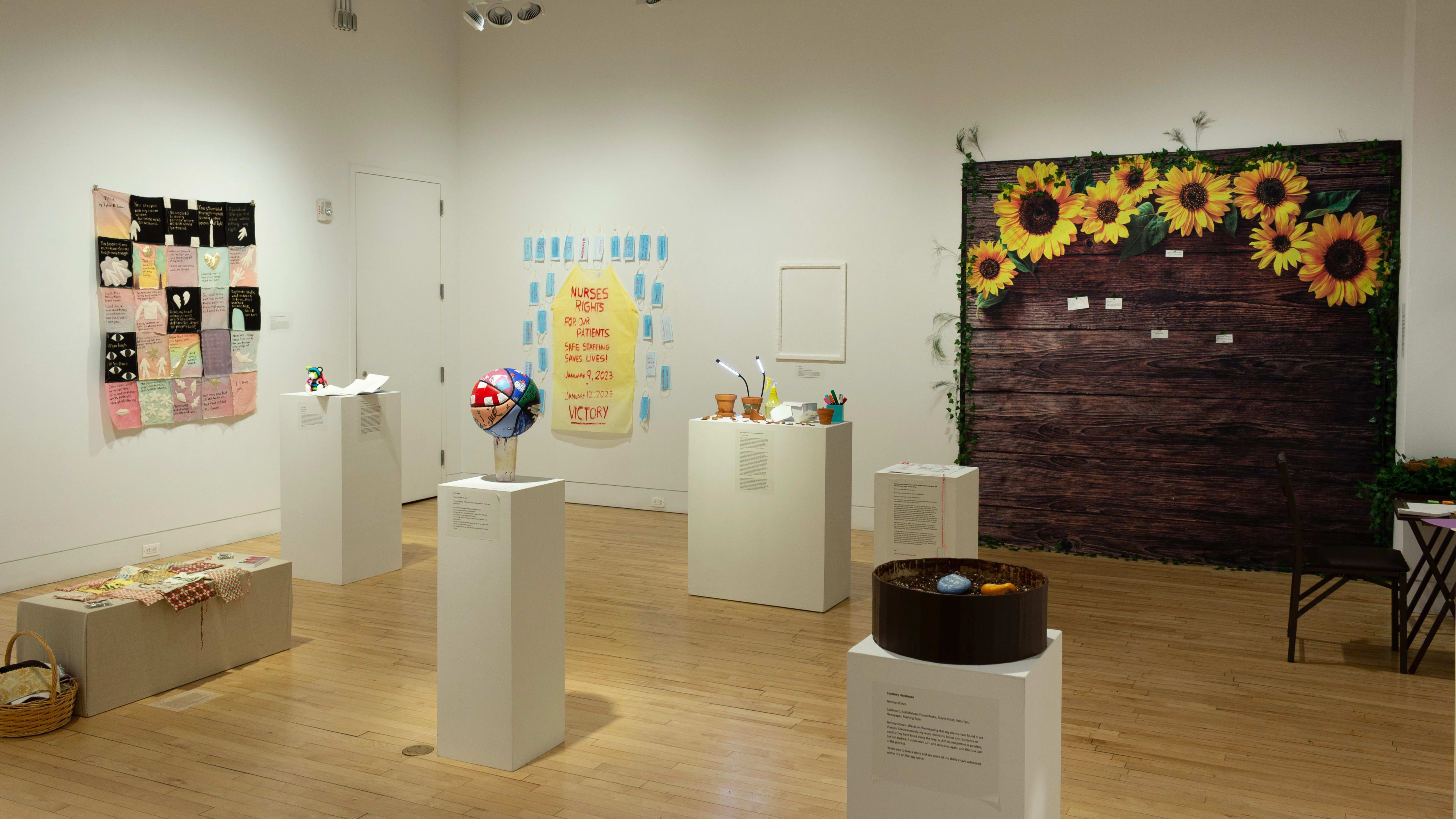 Installation image featuring wall with sunflowers in the background, and 6 pedestals with artwork.