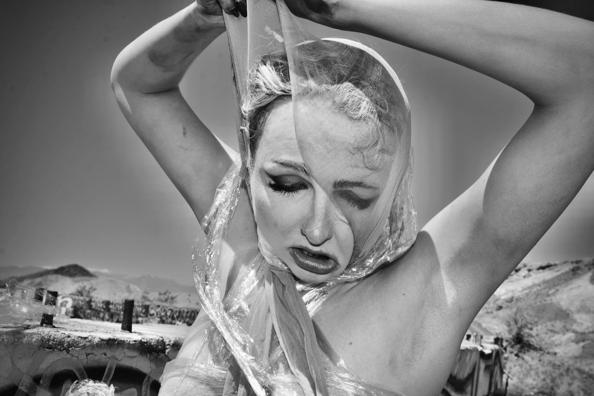 Black and White inkjet photograph of a woman in despair, tearing off pantyhose and cellophane wrap. Takes place in Las Vegas desert. 