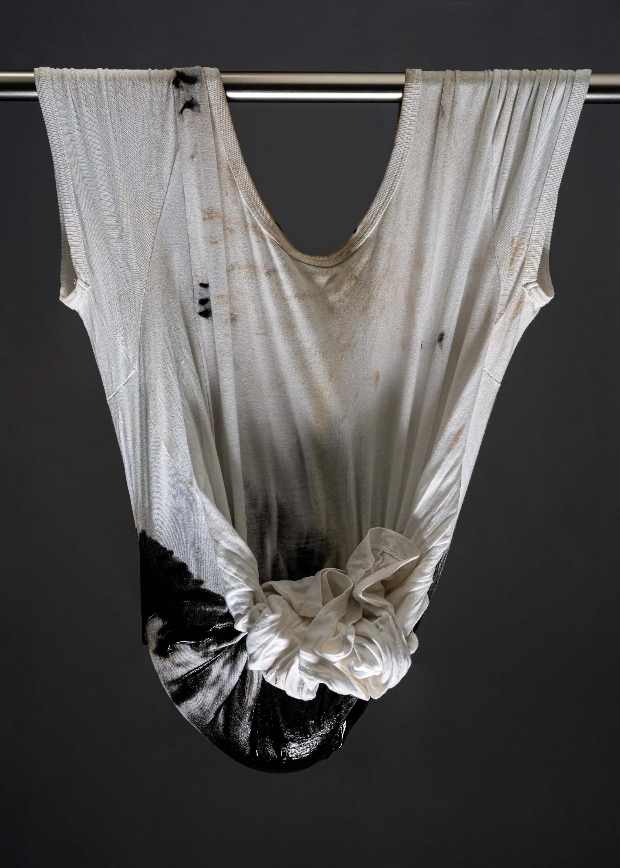 Still life photo of a dirtied white t-shirt hung by a curtain rod, which runs through the sleeve holes